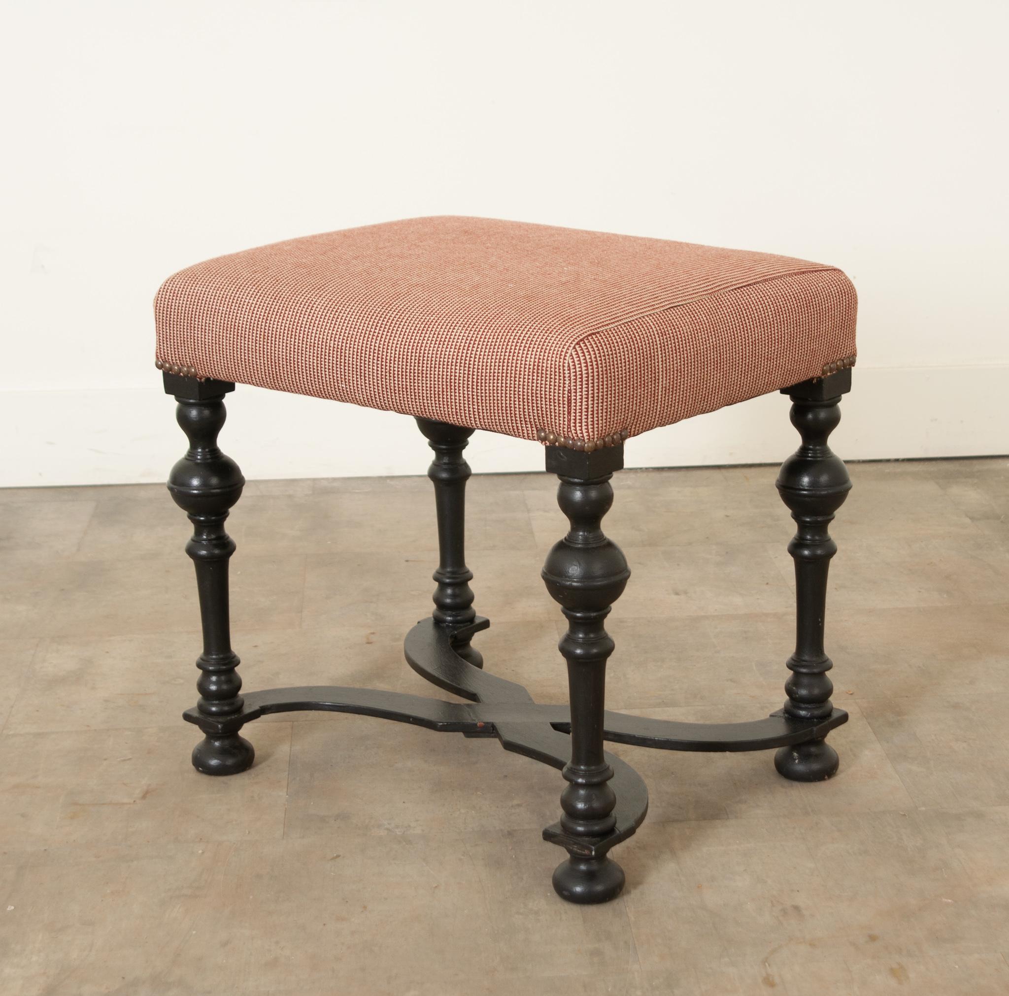 This dignified stool is the perfect antique to add interest to any space. Upholstered with a new deep red and cream patterned fabric and held with new round brass nailheads. The heavy solid painted wood frame showcases hand-carved elements