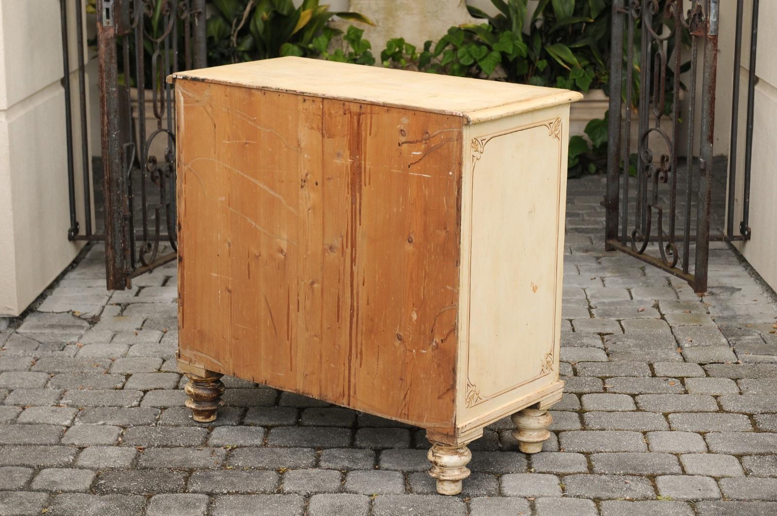 An English painted wood four-drawer commode from the late 19th century, with old paint, new scrollwork motifs and turnip feet. Born in England during the later years of the 19th century, this charming commode features a rectangular top with beveled