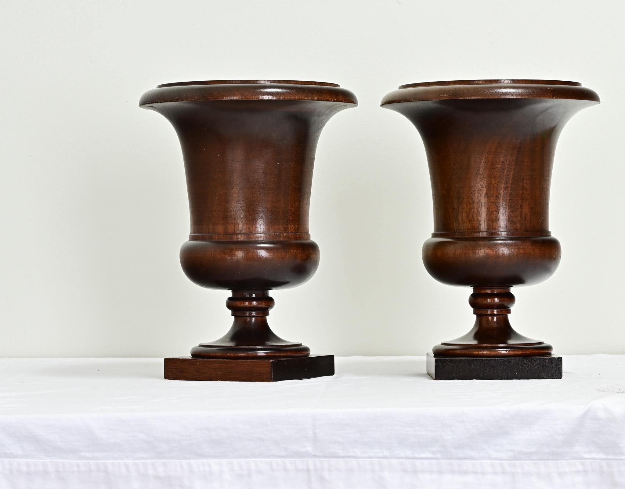 An impressive pair of walnut urns made in 19th century England. These urns have been expertly turned on a lathe to create the basin and pedestal, ending on mahogany square bases. Cleaned and polished with a paste wax, this pair is ready for your