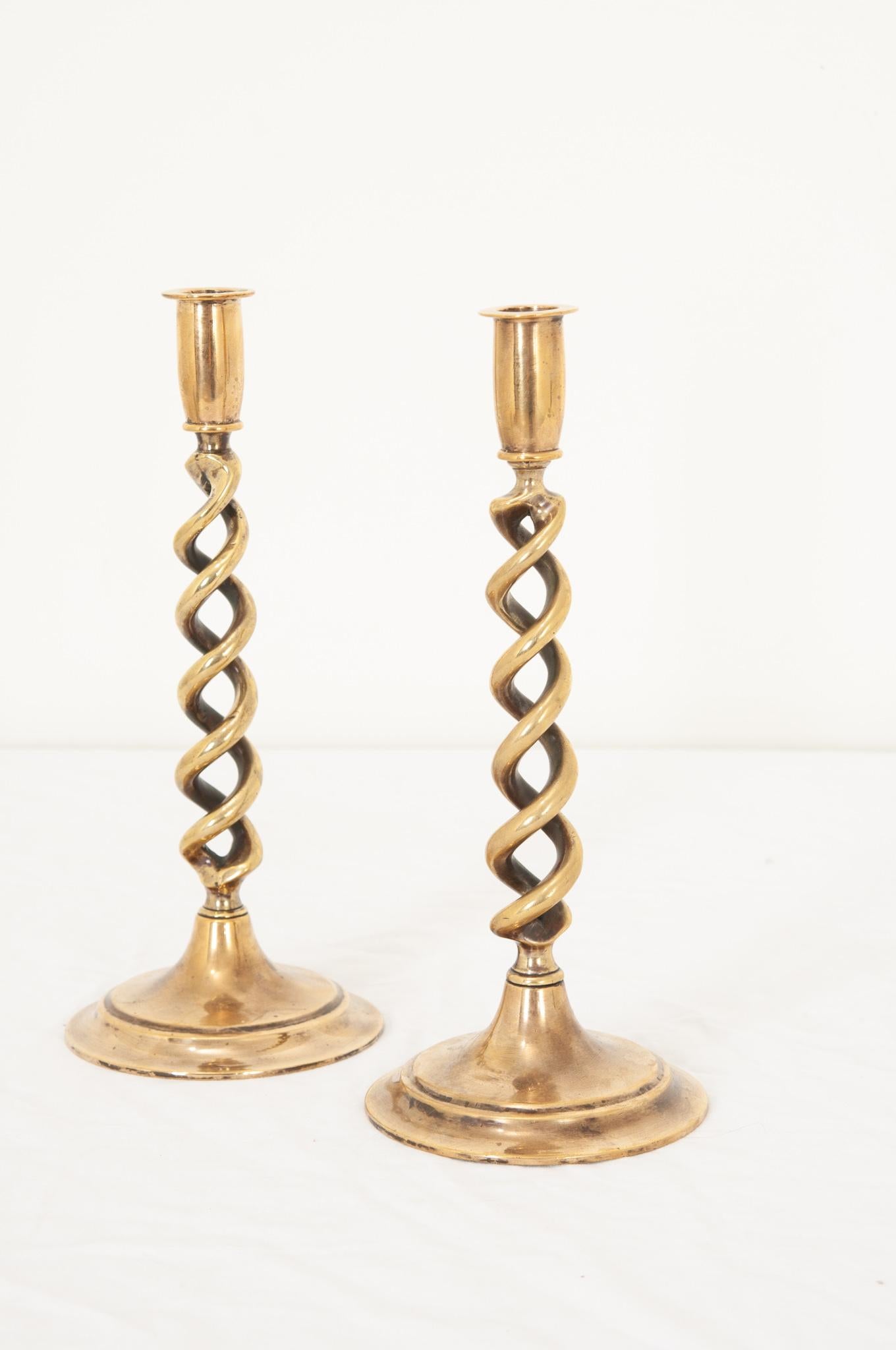 A delightful pair of brass open barley twist candlestick holders hand crafted in England in the 19th century with round circular bases and a lovely aged patina. Quite heavy and of fantastic quality, this pair of candlestick holders will add interest