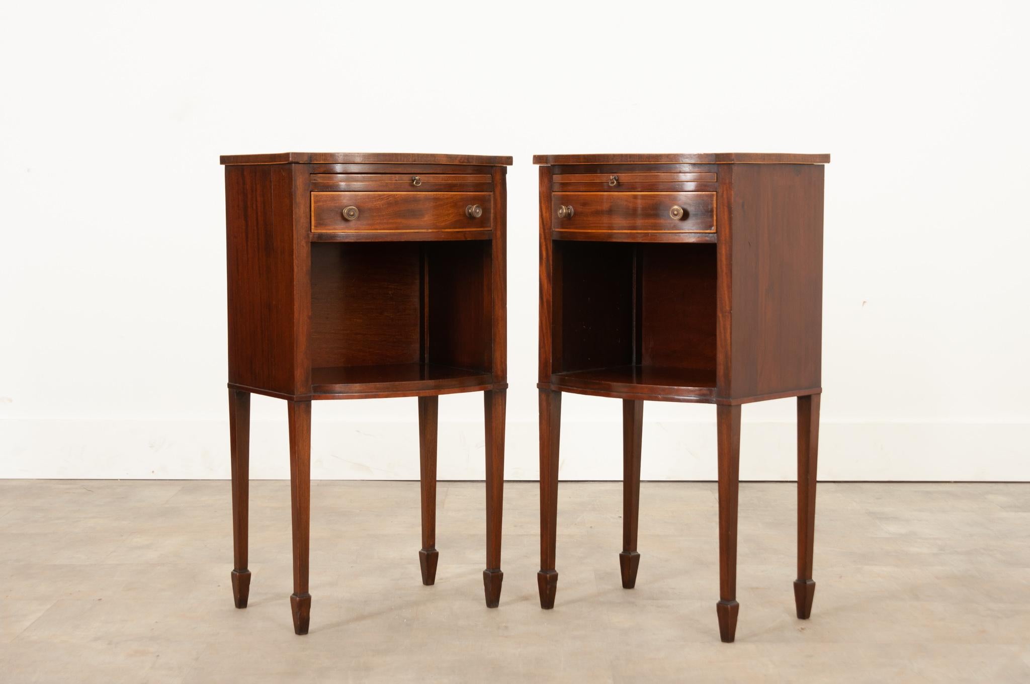 This unique little pair of bedside side tables are wonderfully versatile. Each has a drink slide and slim drawer accentuated with a lighter wood above an open storage space. The mahogany slides are in fine antique condition and fixed with a simple