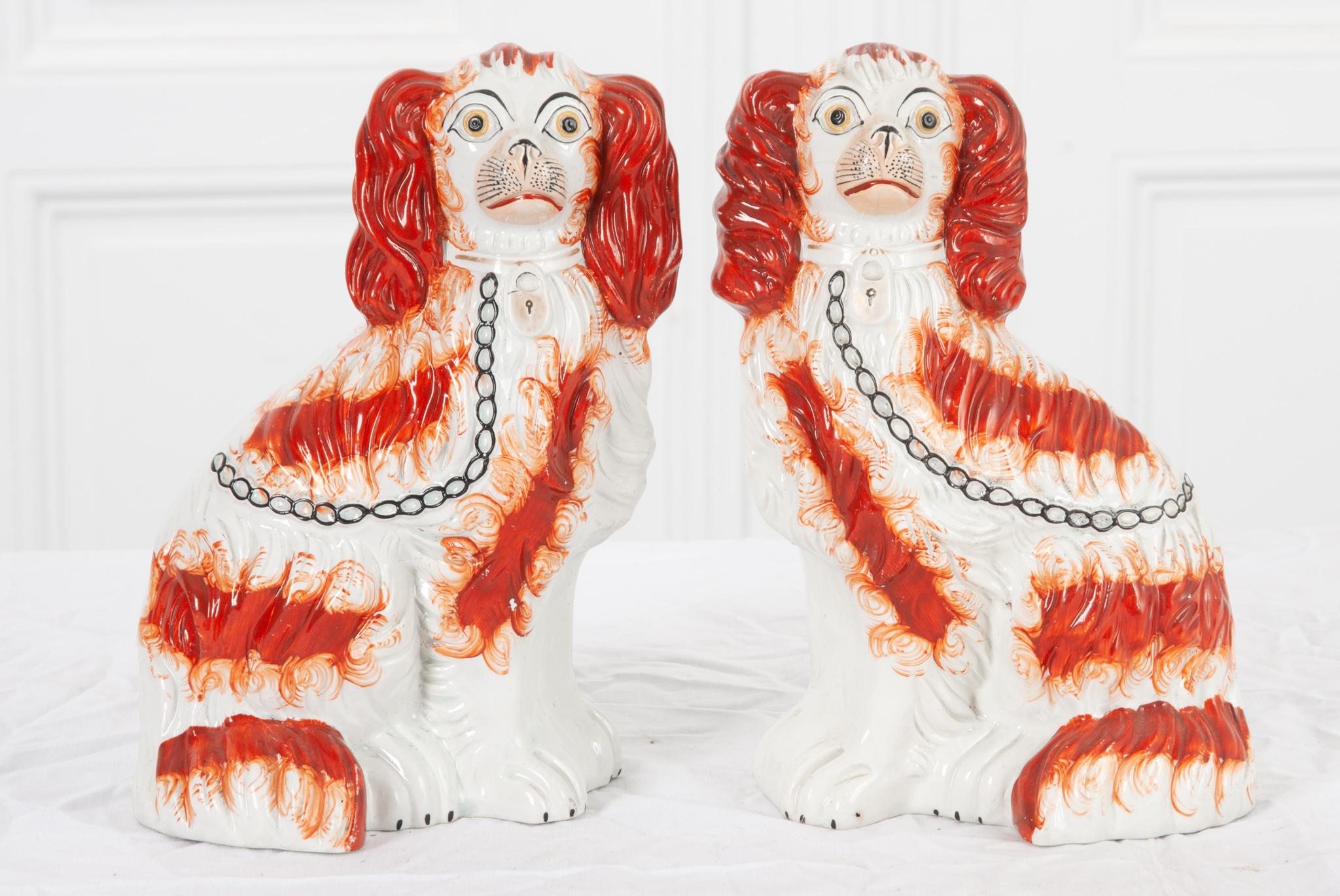 This lovely pair of Staffordshire Dogs are named so for the area in England they originate. Two seated King Charles Spaniel dogs with delicate detail throughout; gold and rust colored fur, a black chain leash, and worn gold collar with a lock. Make