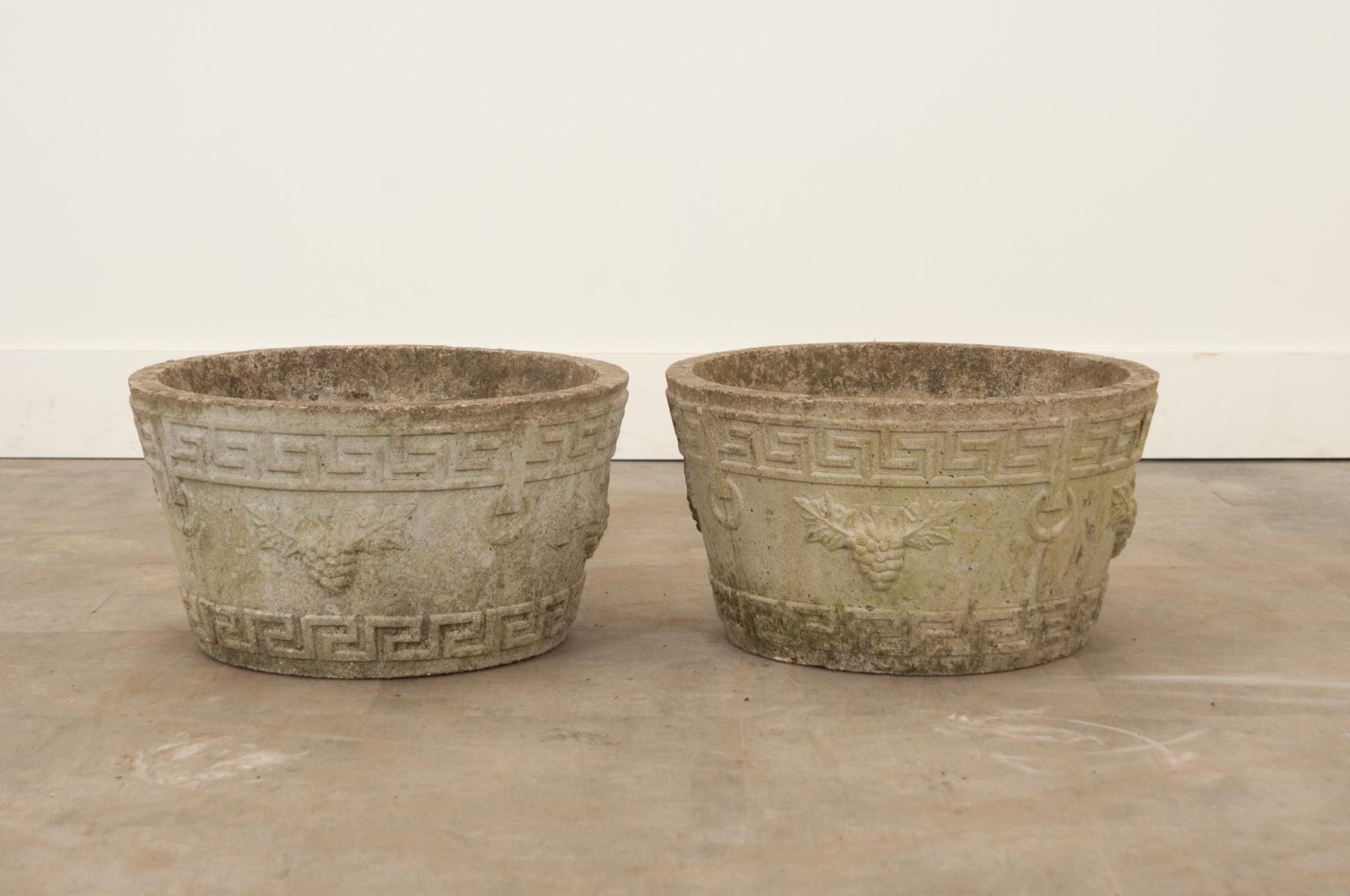 Drawing on classically inspired motifs, this pair of planters showcase Greek key borders and grape vine designs. Years of outdoor exposure have given them a fascinating patina. The bottoms feature holes for water drainage. Make sure to view the