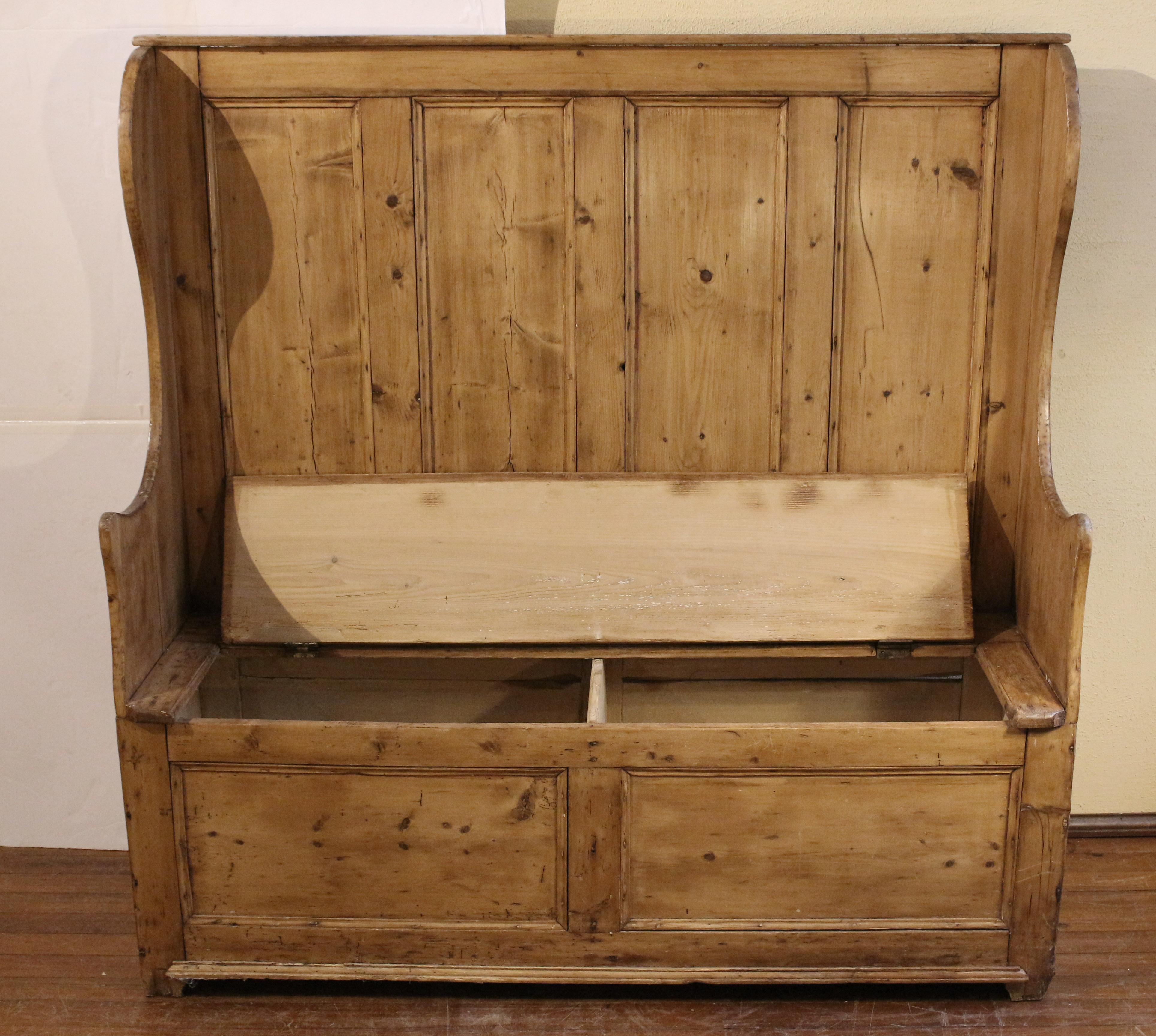 English panel-back winged settle, circa 1830-60, pine. A handsome example with blanket chest seat and the attractive fully paneled back allows use in all locations. The sculpted wings sweep down to create comfortable arm rests. In winter, these