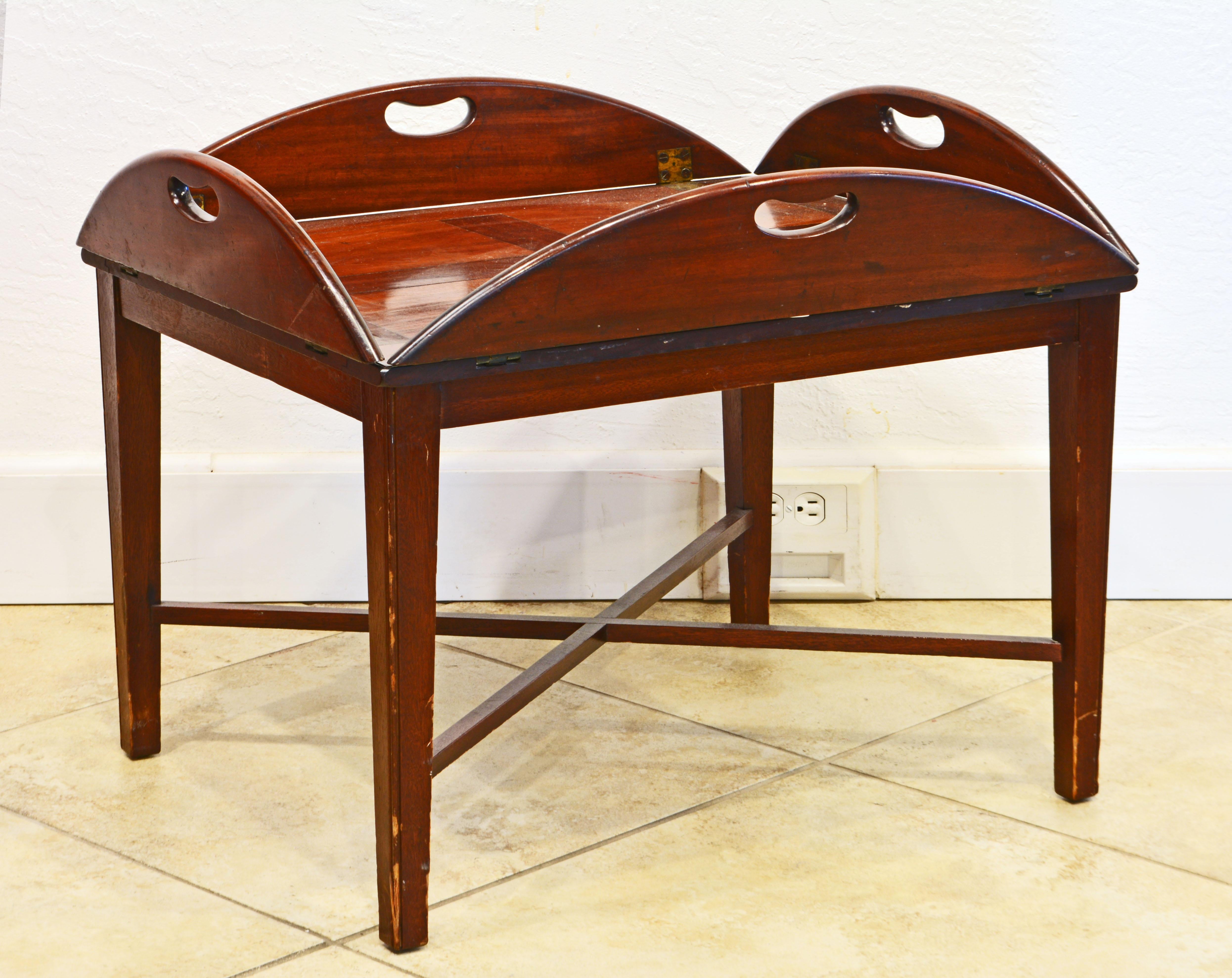 This Georgian early 19th C. mahogany butler's tray of oval form with rectangular paneled center feature brass hinged leaves with shaped open handles fixed on a custom made stand with X-stretcher of a later date creating the ideal coffee table Time