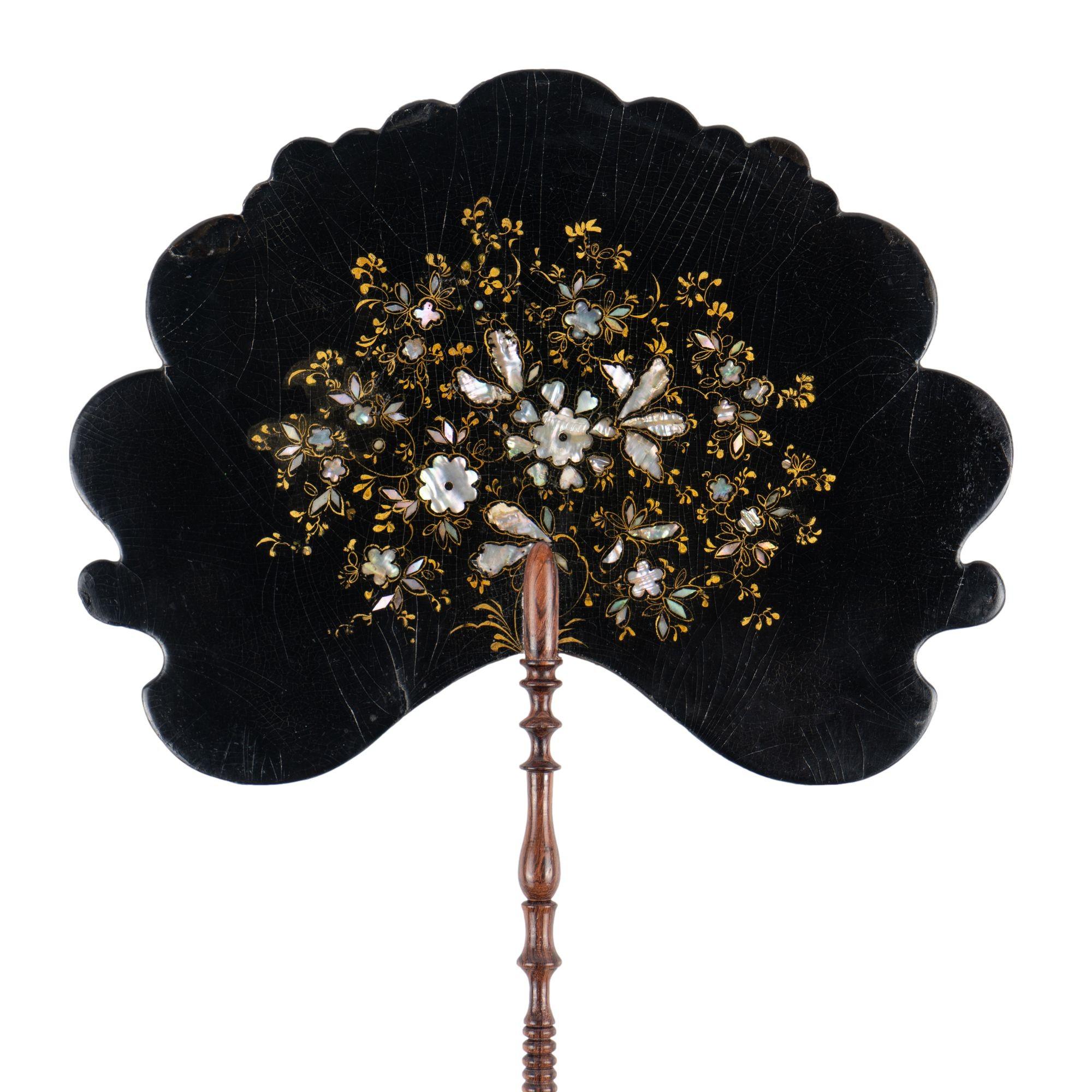 Black paper mache face screen with inlaid abalone and highlighted in gilt with an overall floral spray. These screens were used by women to shield their face from the heat as they sat close to the fire in colder months. The fan is mounted on a