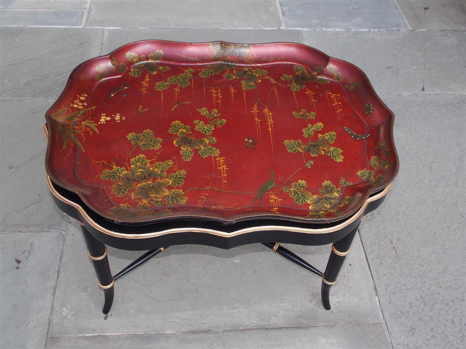 English paper mache red lacquered scalloped tray with decorative bird, butterfly, dragonfly, and foliage motif resting on a faux painted and gilt bamboo stand with splayed legs and the original connecting stretchers, Early 19th century.