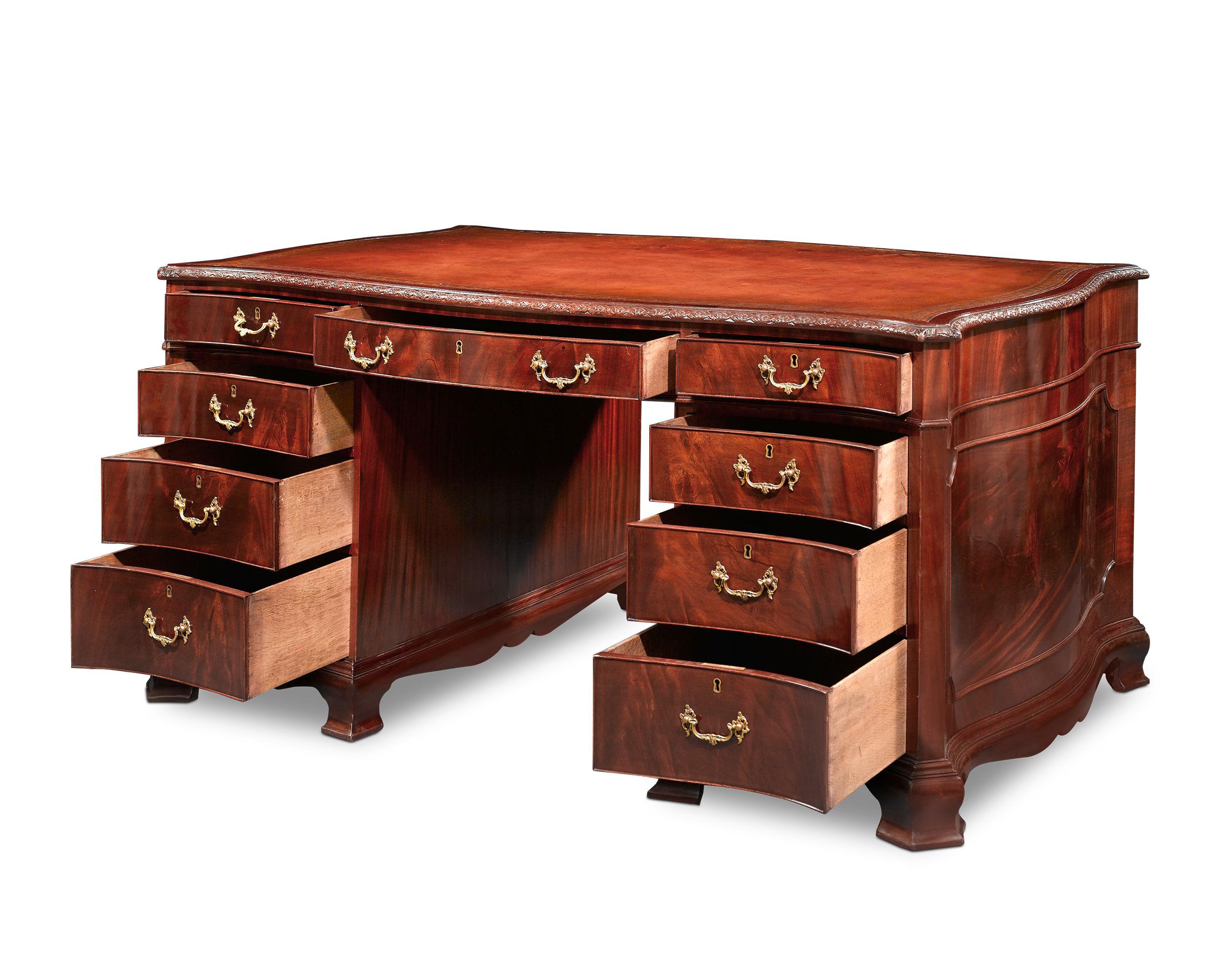 This handsome English partner's desk is expertly crafted with classic serpentine edges and bracket feet. Designed for dual use, each side is identical in appearance, with one side of the desk equipped with drawers and the other with hinged cabinets.