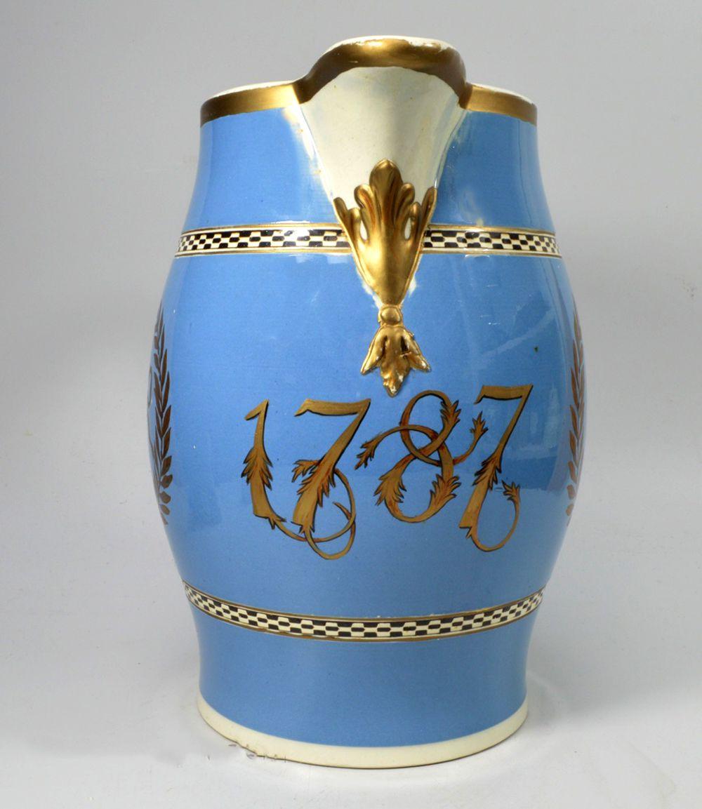 English Pearlware Pottery Large Blue Slip Jug,
Dated 1787,
Possibly Leeds.

The large English pottery light blue slip jug is painted with gold detailing with a date of 1787 below the spout.  On one side a large stag head crest within a laurel leaf