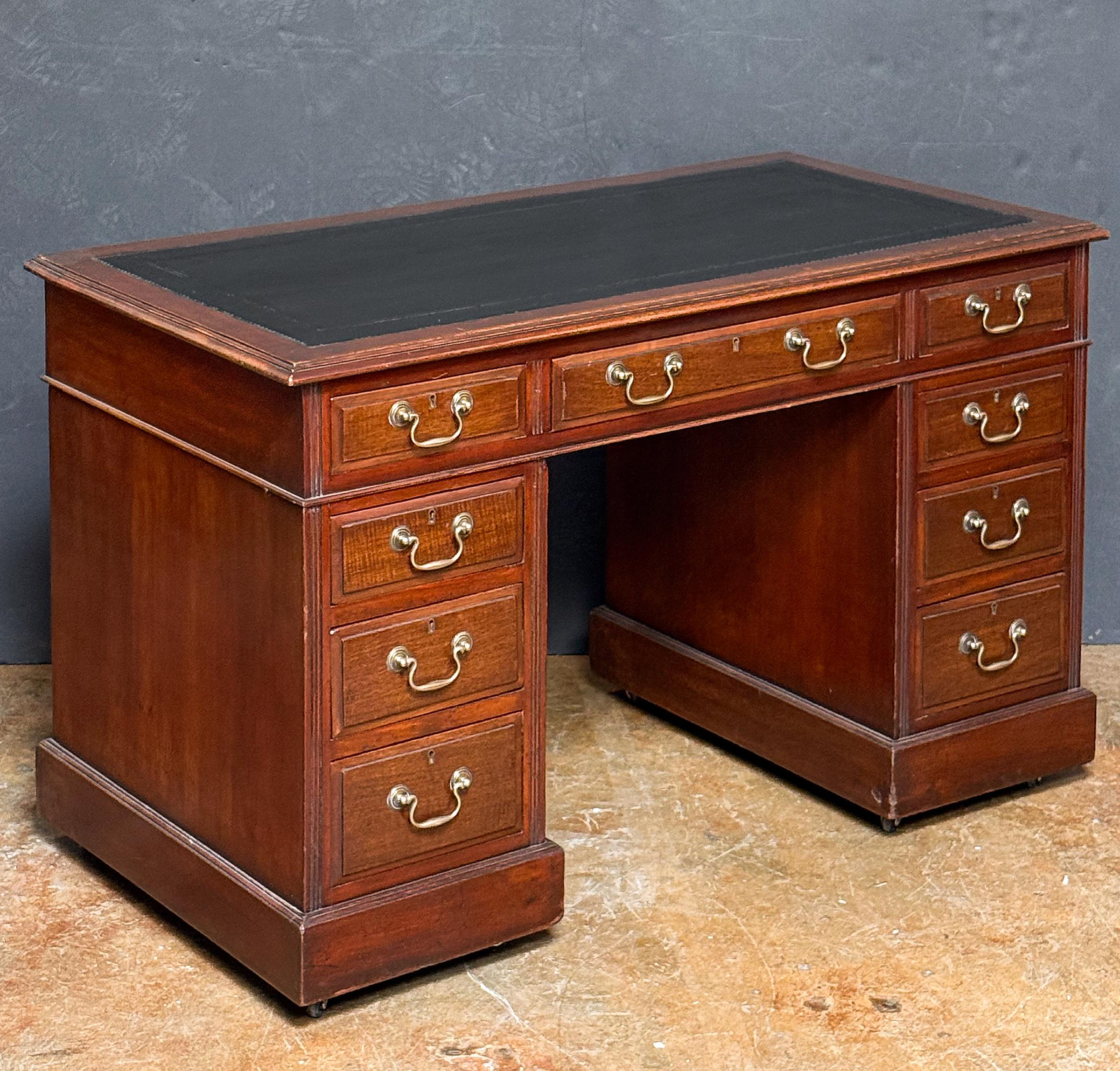 A fine English double pedestal desk of mahogany from the Edwardian era, featuring a leather-inset top in black with mahogany surround, over a frieze of one long drawer between two opposing small drawers, set upon two pedestals. 
Each pedestal with