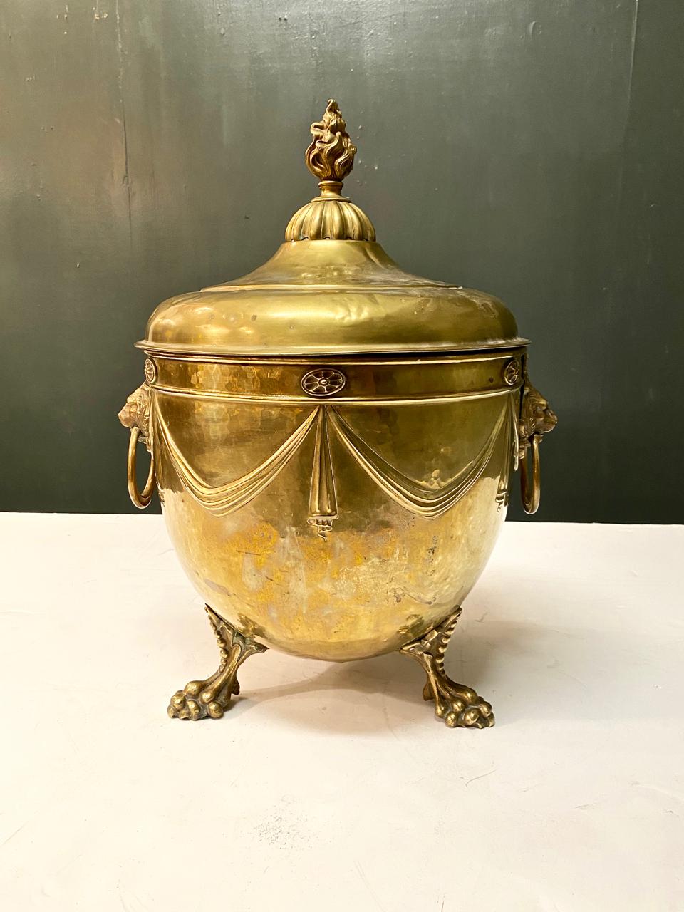 This is a superb example of a brass Regency Purdonium or coal scuttle that dates to c. 1800-1825. The base features highly detailed cast brass lion-head handles and chiseled articulated lion paw feet. The vessel is surrounded by neoclassical drapery