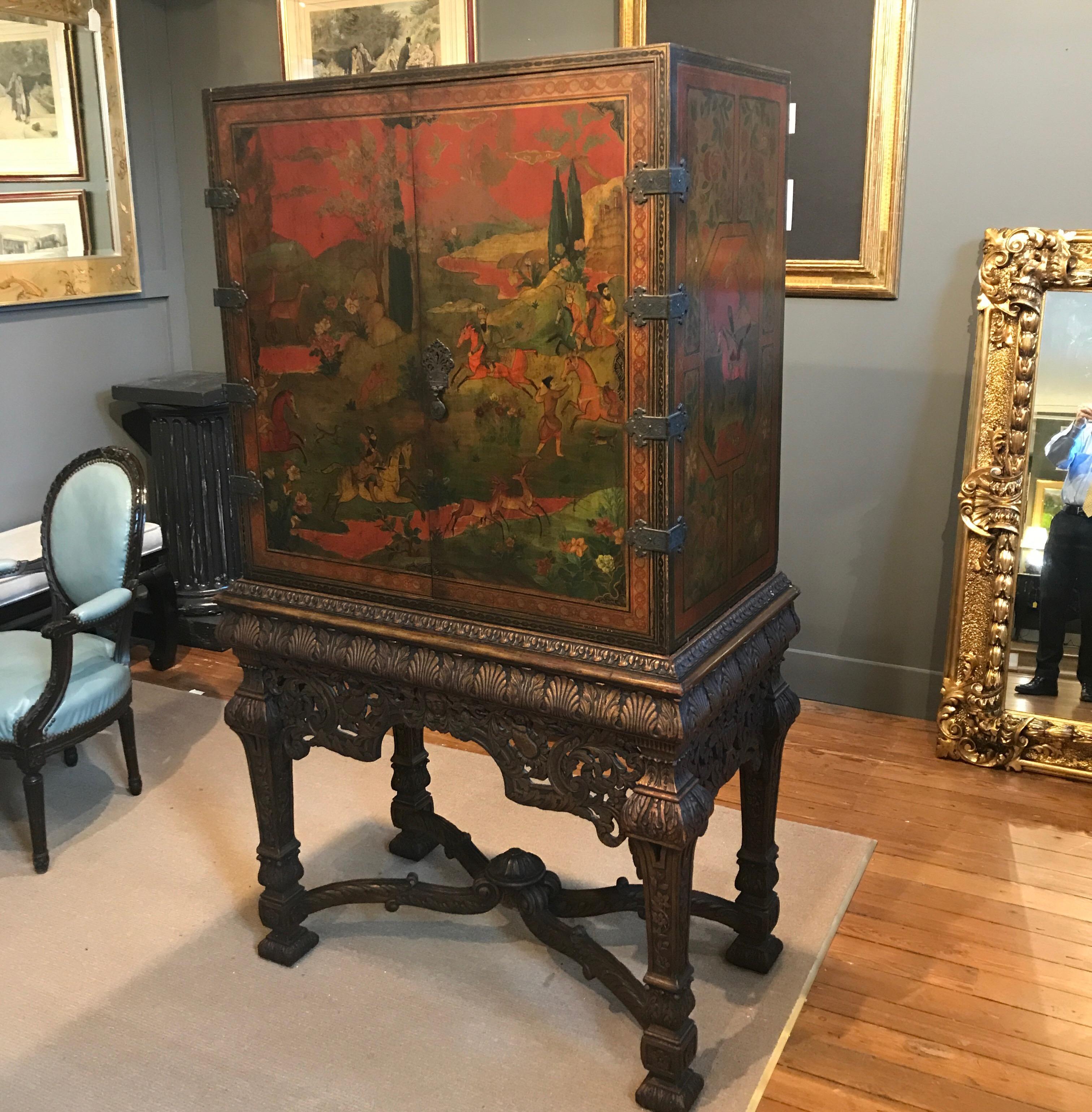 Beautiful hand painted cabinet with hand carved parcel giltwood base. The Persian red top with elaborate Persian hunting scenes with all-over aged gold highlights. The interior opens to reveal the inside doors painted with illuminated floral