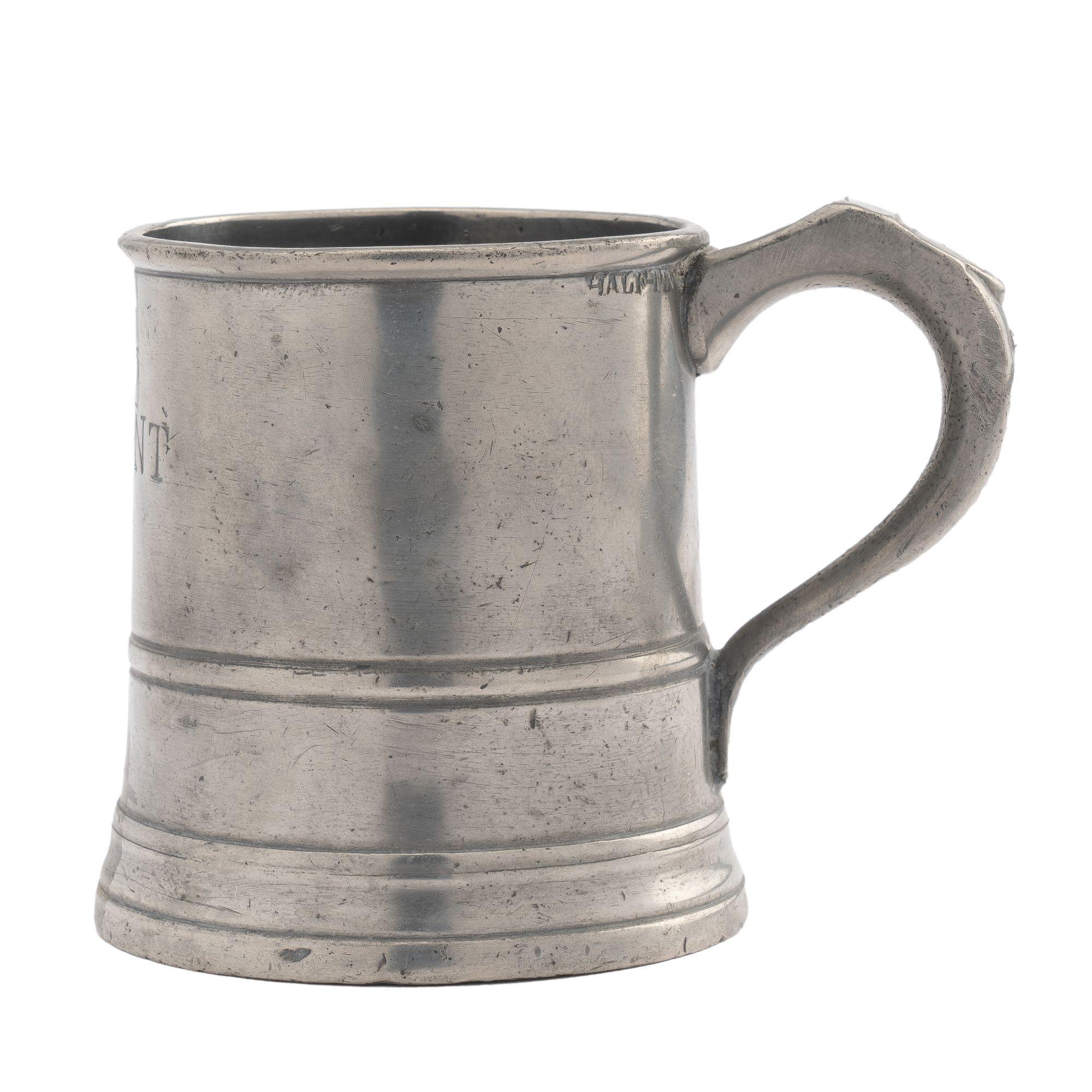 Mug anglais en étain estampillé avec la mesure 1/2 PINT. La tasse a un bord perlé et est entourée d'une perle à 2/3 du bord. La base est ornée d'un bourrelet et d'une moulure en ogee qui s'étendent au-delà du fond de la tasse. La poignée à boucle