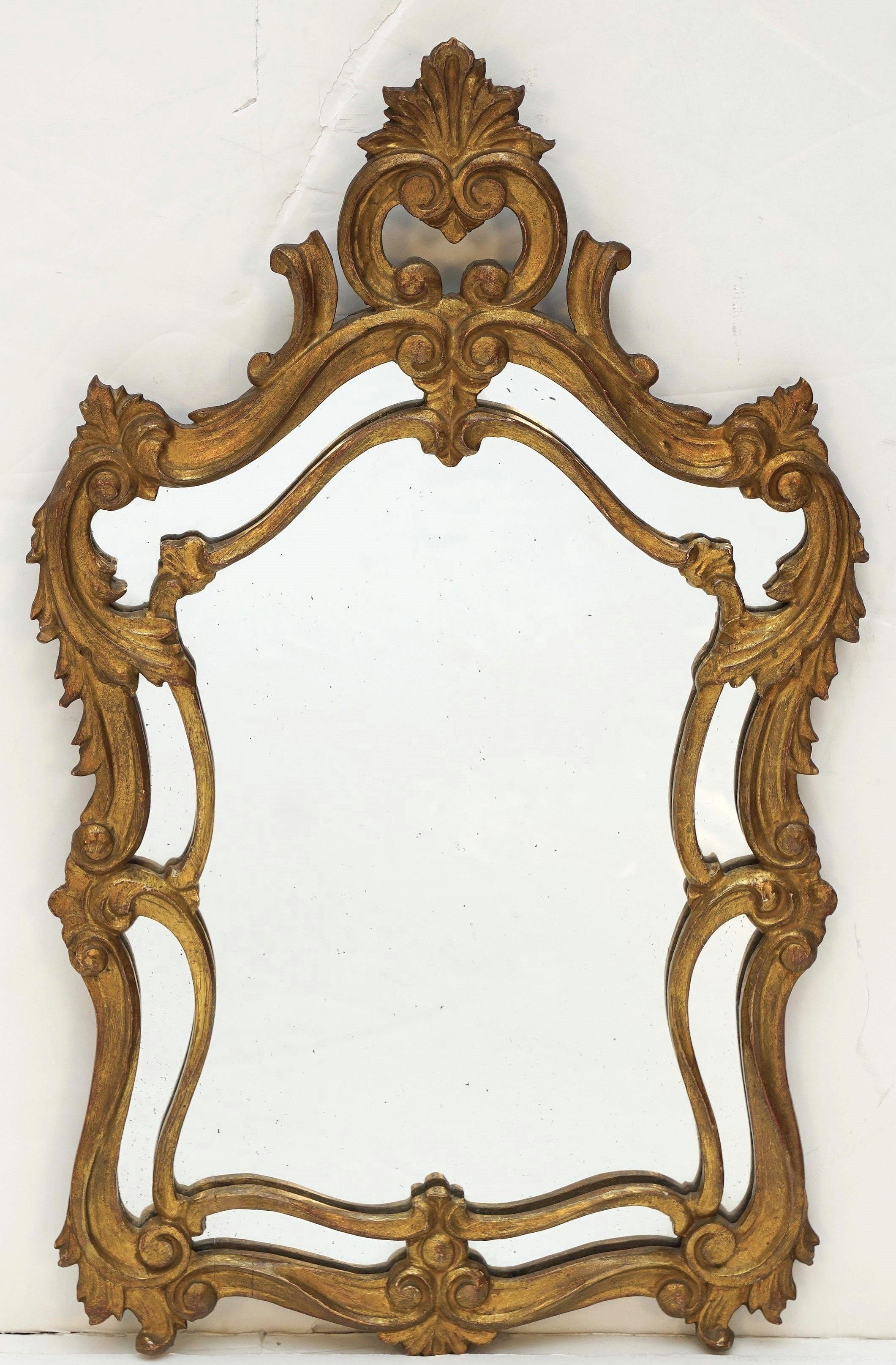 A fine English gilt wall mirror in the Rococo style, featuring a frame with decorative scroll motifs inspired by the classical tradition around the circumference, with a crest accent crowning the top.

Dimensions: H 30.75 in x W 18.5 in x D 2 in 