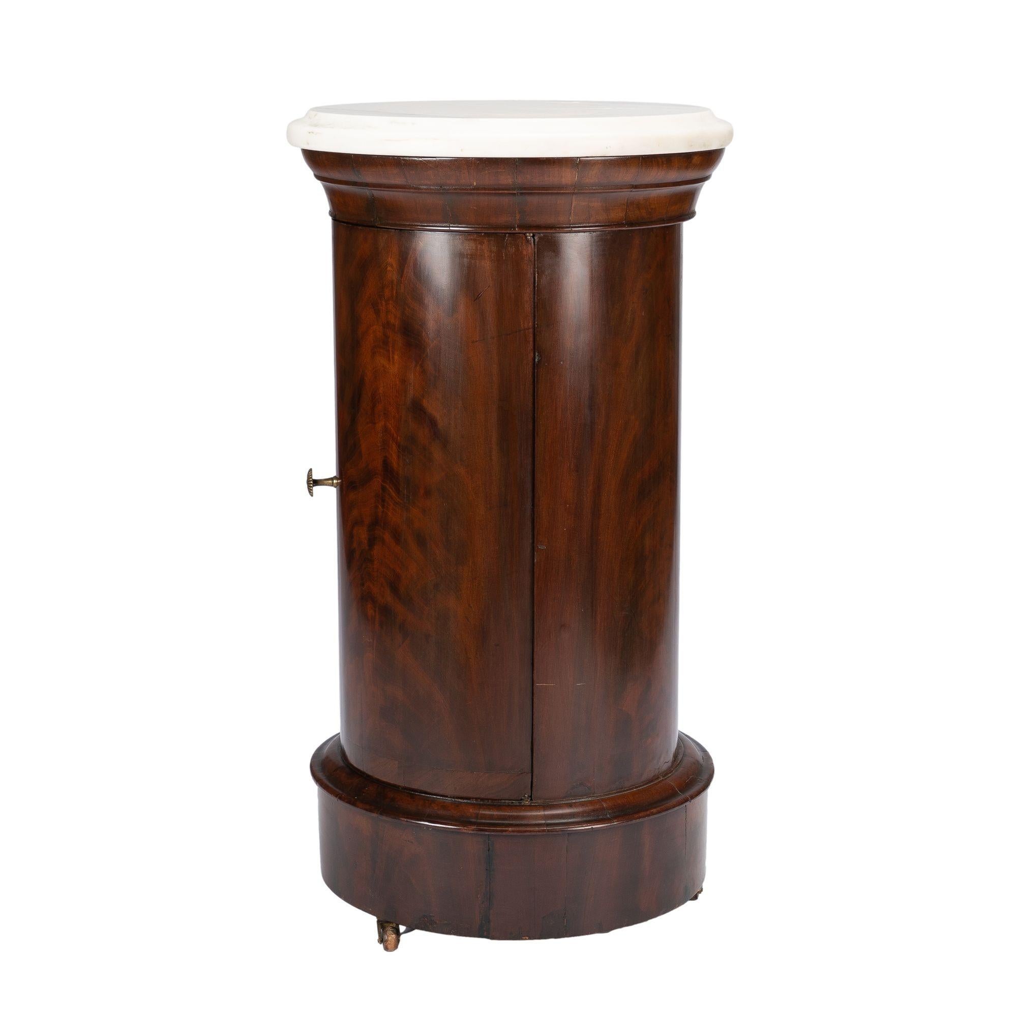 Mahogany pillar commode with a solid marble circular ogee edge top. The columnar shaft of the commode is fitted with two interior shelves, and the whole piece rests on a base molding with three brass castors. The commode is in fine original