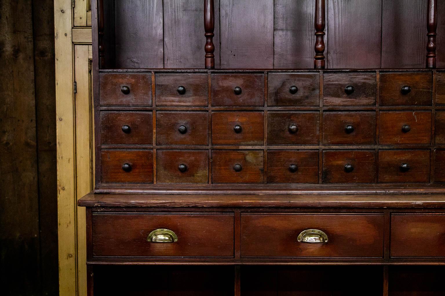 The top section of this apothecary cupboard has thirty apothecary drawers with the original wooden knobs. The top has eight support columns with matching pilasters on the sides. The drawers on the top and bottom both have incised cockbead. The