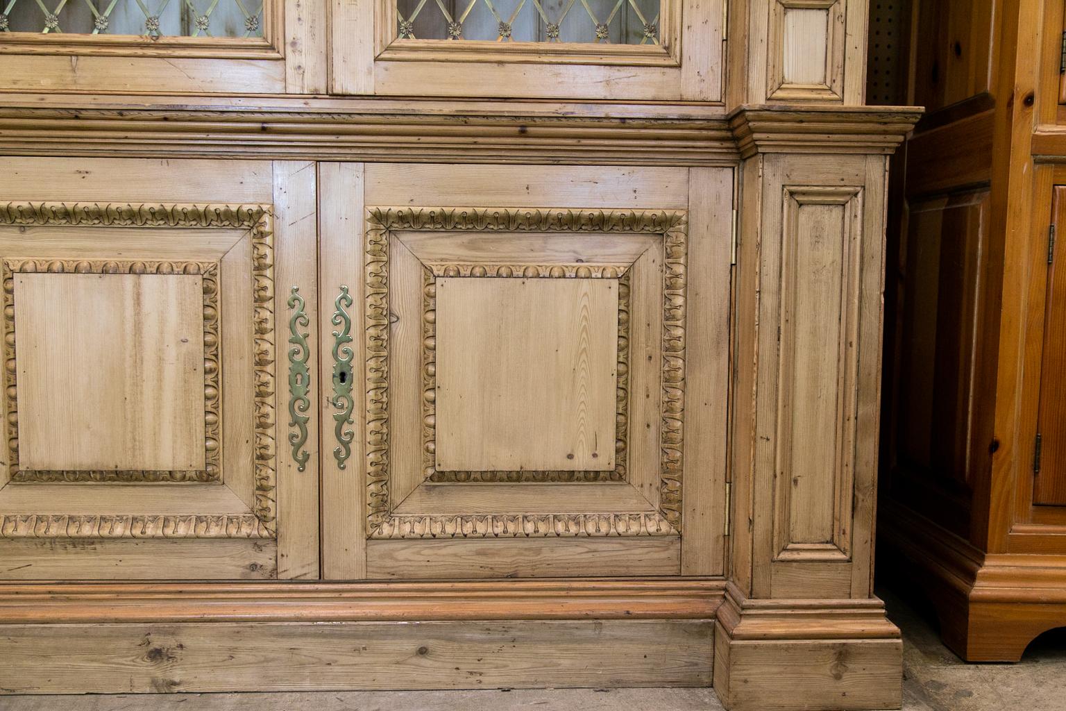 English pine bookcase, with multi piece architectural cornice, Corinthian style capitals above fluted pilasters. The lower panel doors with egg and dart and leaf moldings. The upper doors have grills with solid brass floral rosettes. The shelves are