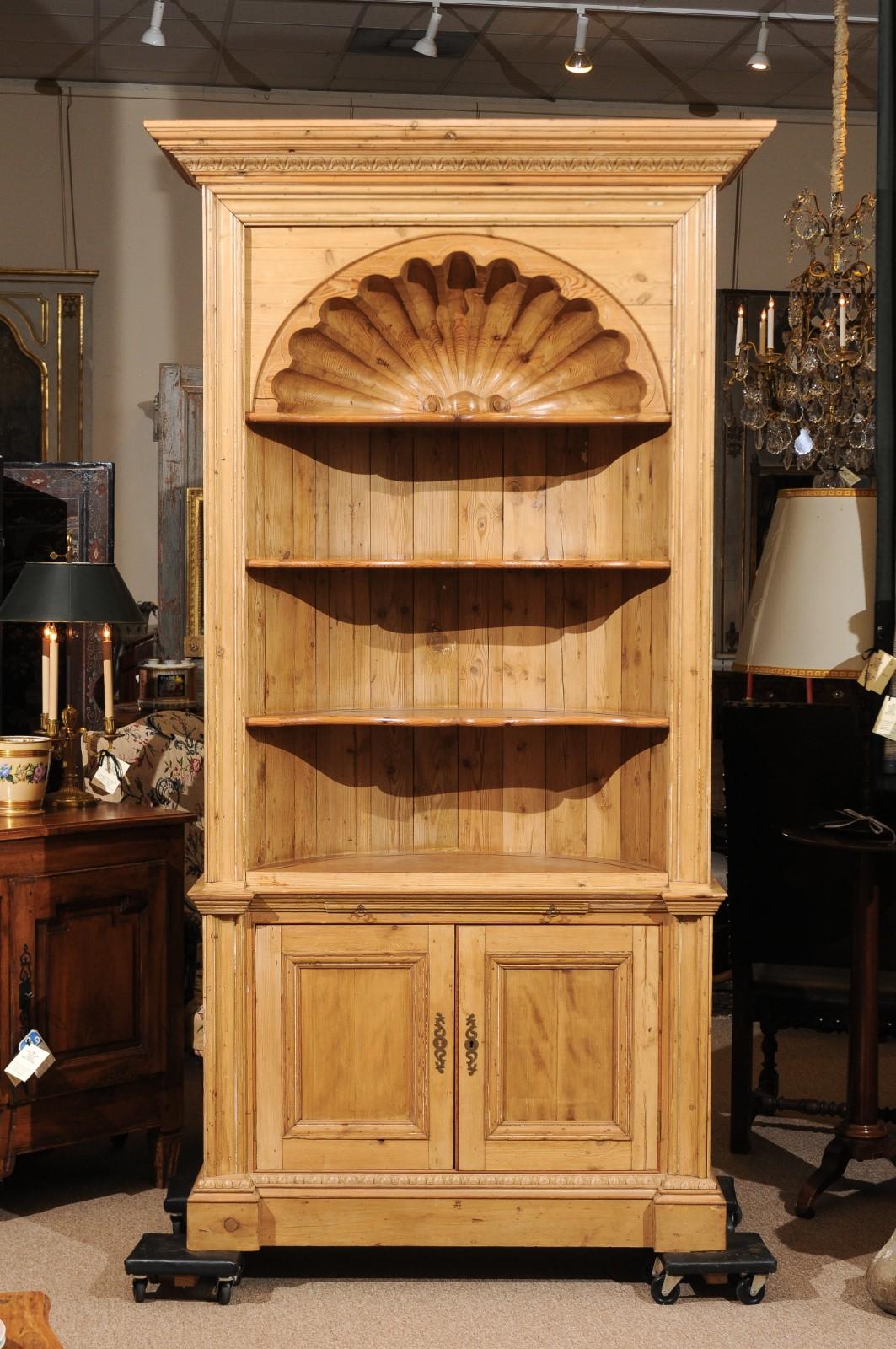 An English pine bookcase featuring shell carving 3 shelves and 2 paneled door cabinet below. The cabinet composed out of old pine elements.