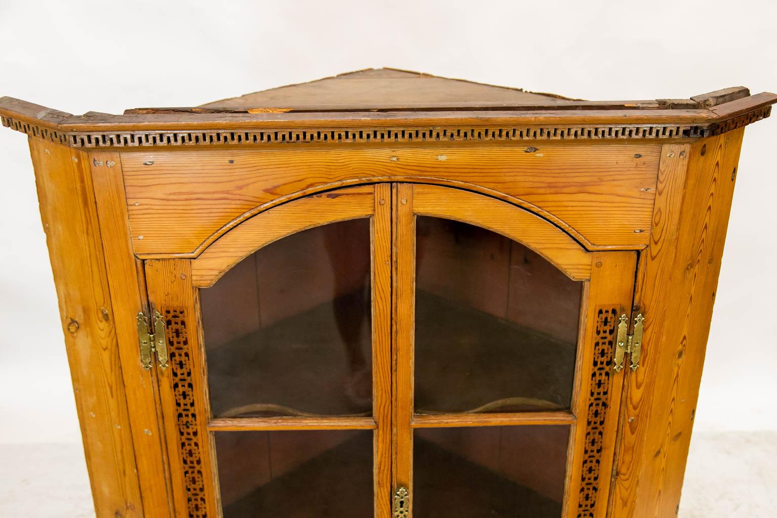 This corner cupboard has exposed peg construction. The cornice has the original wall of Troy molding. The front stiles have pierced open work carvings. The interior shelves have two fixed butterfly shelves. The blown glass is original.