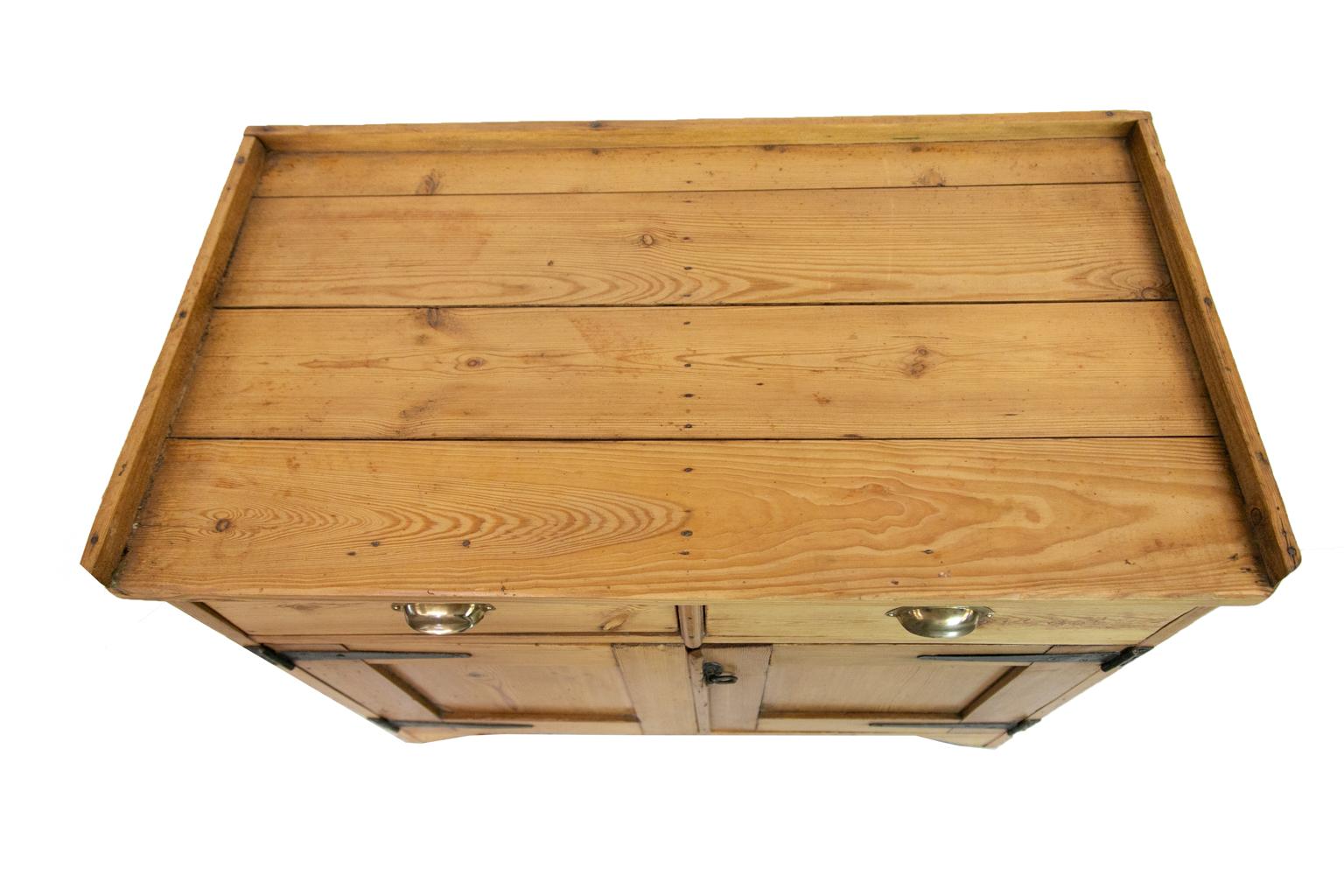 Este servidor rural de pino inglés tiene una galería de una pulgada que rodea el lomo y los laterales. Hay una encimera de cuatro tablas con separaciones entre ellas. Los cajones tienen tiradores de latón. Las puertas tienen grandes bisagras de
