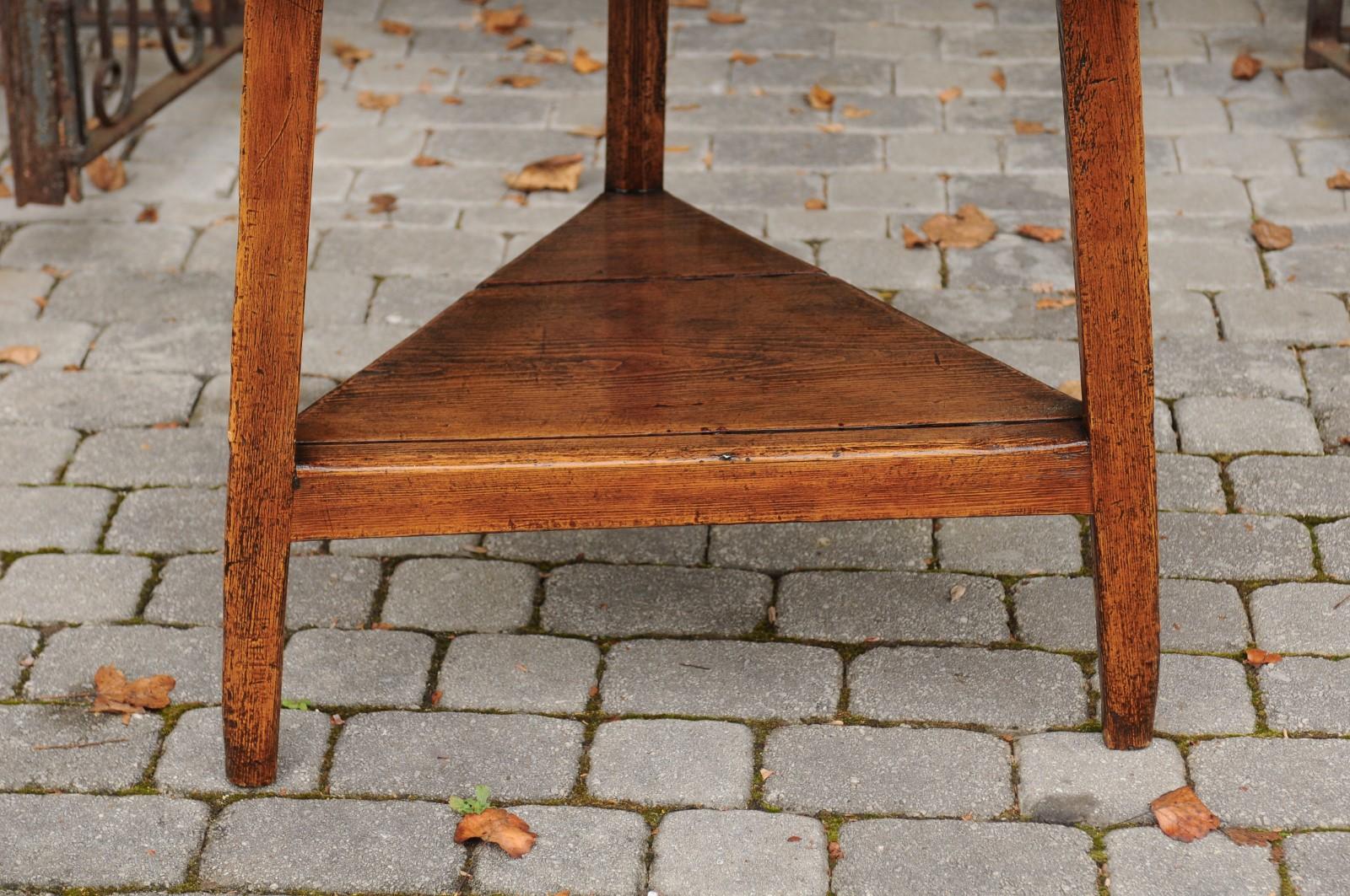An English pine cricket table from the second half of the 19th century, with circular top, triangular shelf and straight angled legs. This rustic cricket side table features a round top, sitting above a simple triangular apron, echoing the shape of