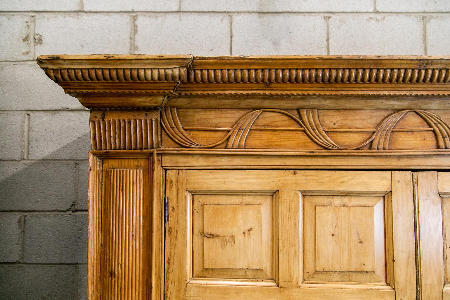 Armoire anglaise en pin, avec une belle corniche sculptée et des vagues sculptées dans la frise. La corniche cannelée est ornée de pilastres cannelés et de panneaux latéraux.