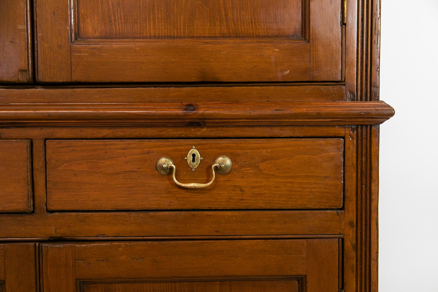 This pine cupboard has exposed peg construction. The top and bottom doors have recessed molded panels. The upper and lower side stiles have carved reeding which terminate in ogee feet.
  