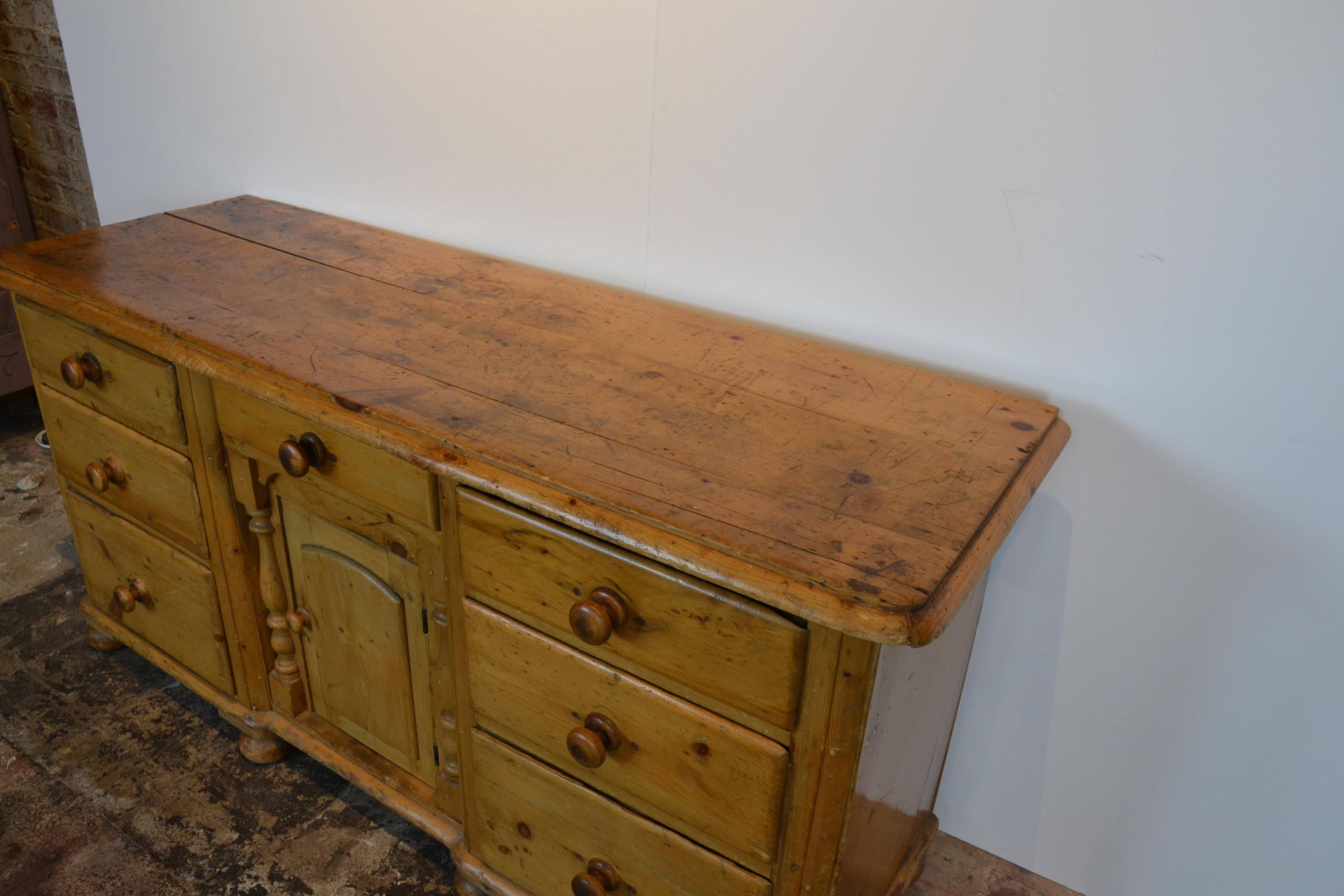 An English 19th century pine dresser base or sideboard. Bun feet. Features 7 drawers with a center cupboard with a solid center panel and surrounded by half-pillars. Great old patina to the top, circa 1850.