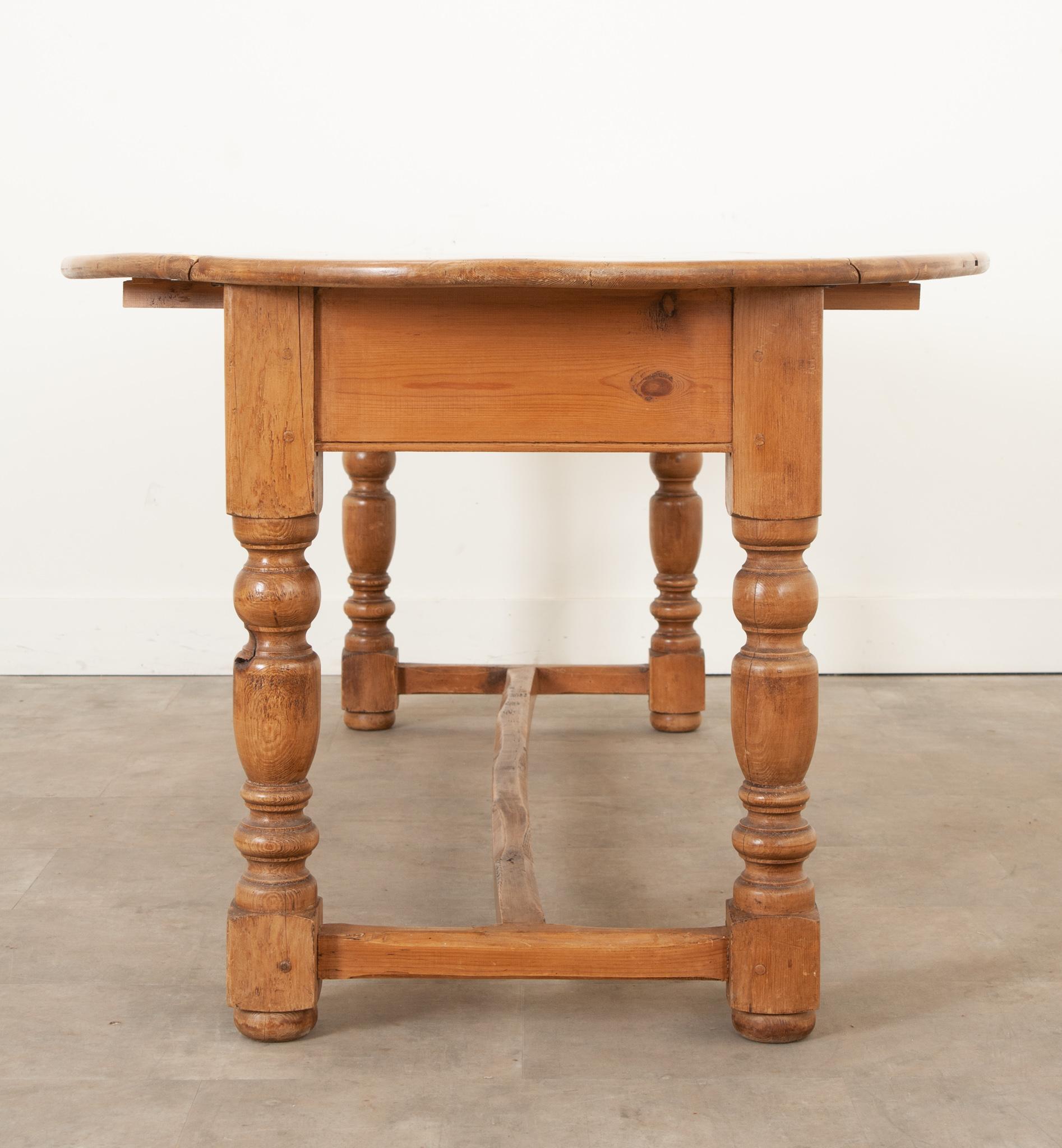 An English drop leaf dining table made of solid pine. This dining table can be used as a console or a dining table. Four turned pine baluster legs are connected with a sturdy stretcher which adds character to this classic dining table. The drop
