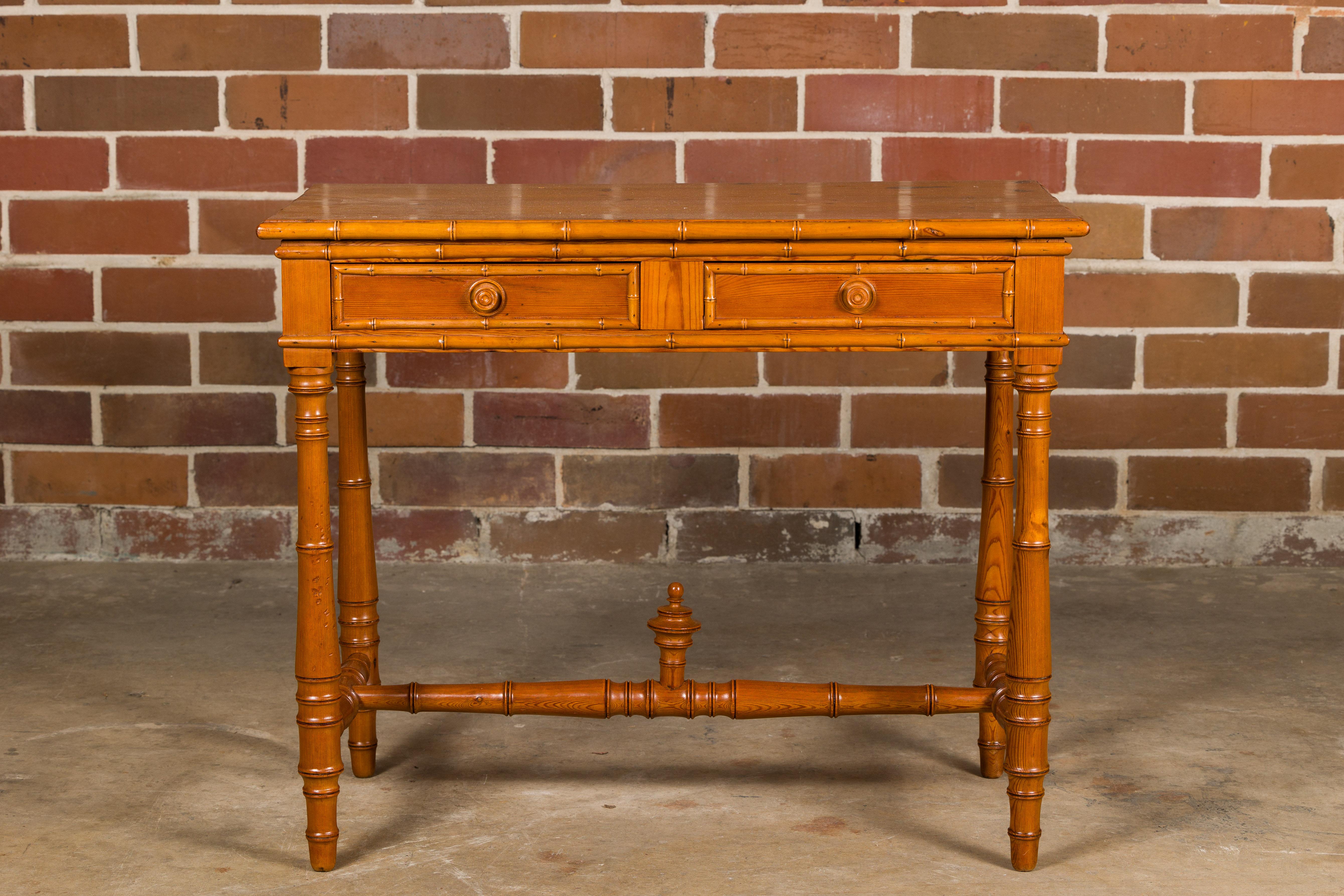 An English pine faux bamboo desk with two drawers and cross stretcher. Introduce a touch of rustic charm and timeless elegance to your home with this exquisite English pine faux bamboo desk. Its warm pine patina exudes an aura of authenticity and