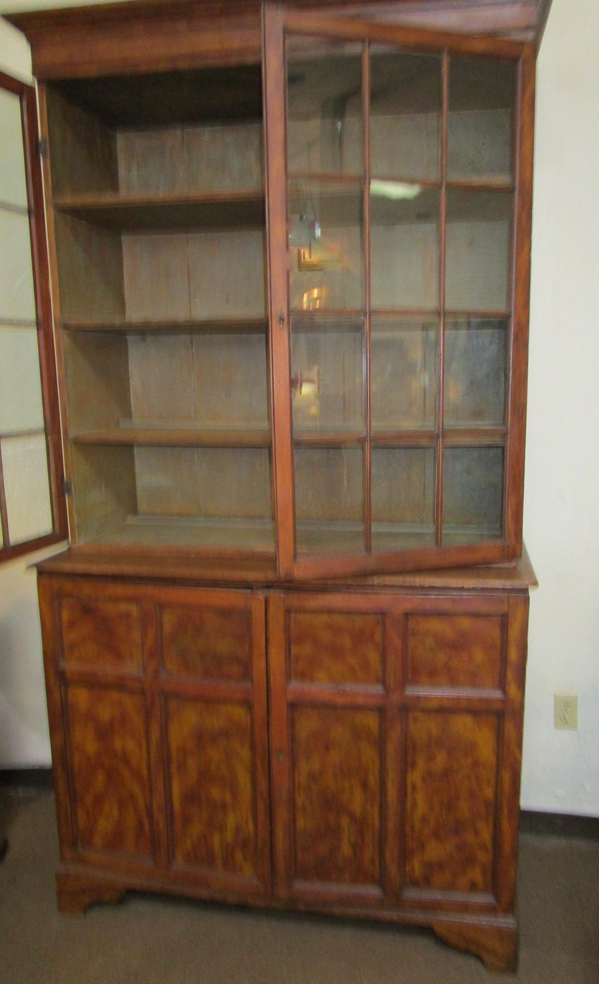 This unusual English pine cupboard is faux painted to resemble mahogany and features the original 24 hand blown wavy glass door panels. There are four shelves at the top and two deep shelves on each side of the closed door panels at the bottom. The