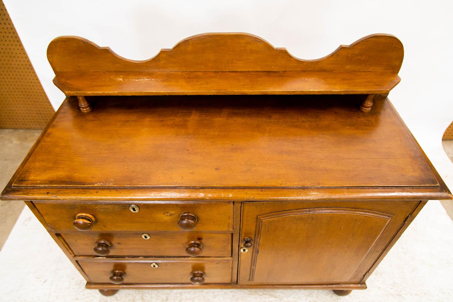 This server has a scalloped rear gallery that has a 4 1/2-inch shelf supported by short turned columns. It has been painted to simulate light oak. The door has a raised arched panel framed with a molded edge. All hardware is original except the