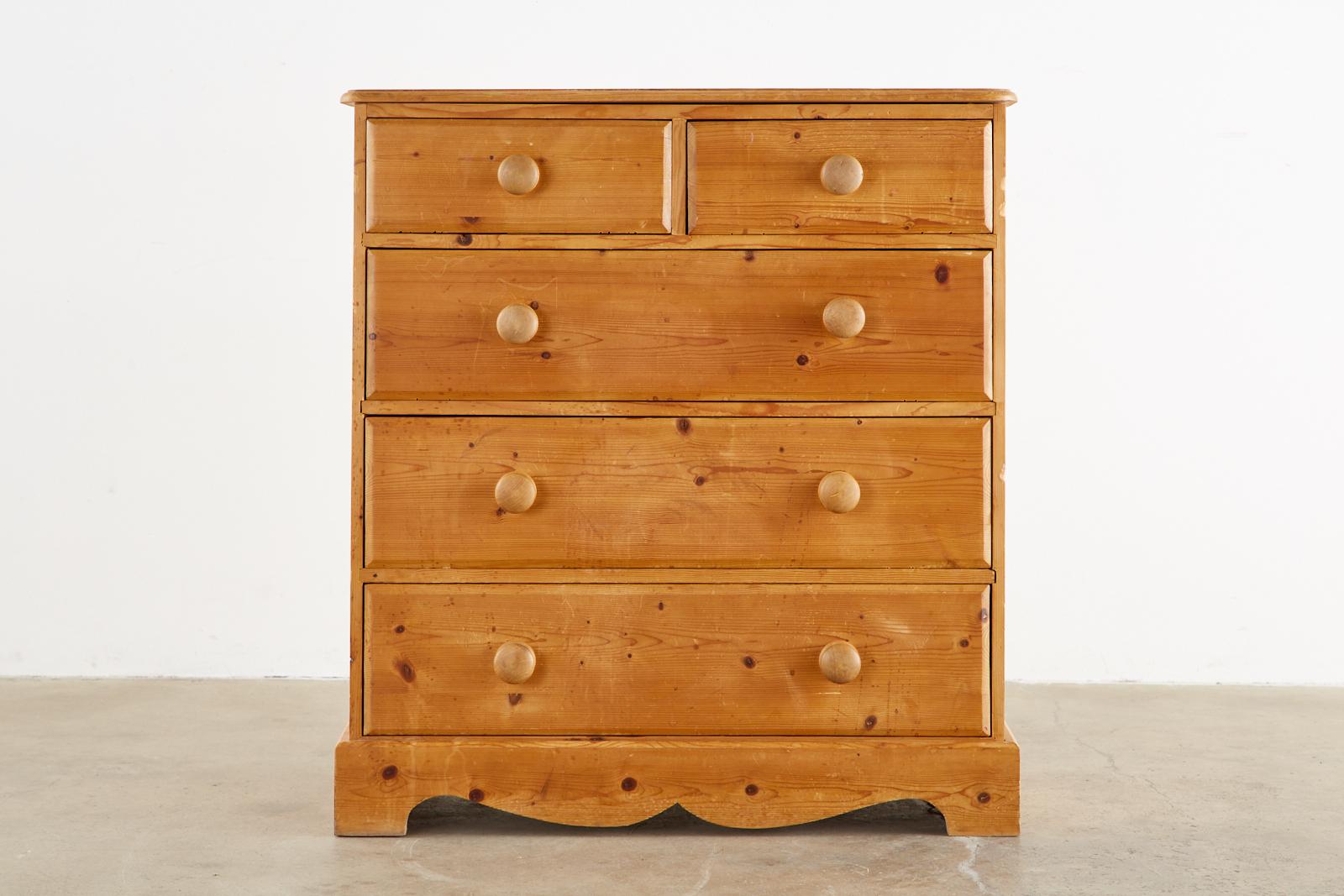 Rustic English pine five-drawer dresser commode or chest of drawers featuring a natural patina. Simple and sturdy with round wood pulls on the drawers. The front has bracket feet with a shaped apron.