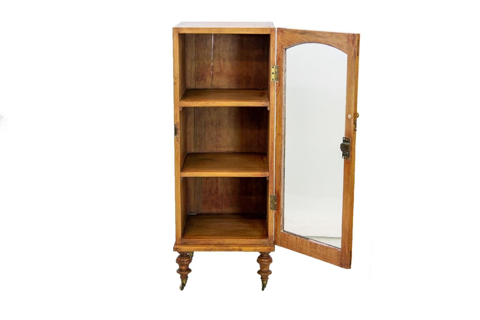 English pine glass door cupboard, the glass front is the original large wavy glass pane. The legs, castors, and hinges are also original. The door has an arched top as well as exposed mortise and tenon construction.
 