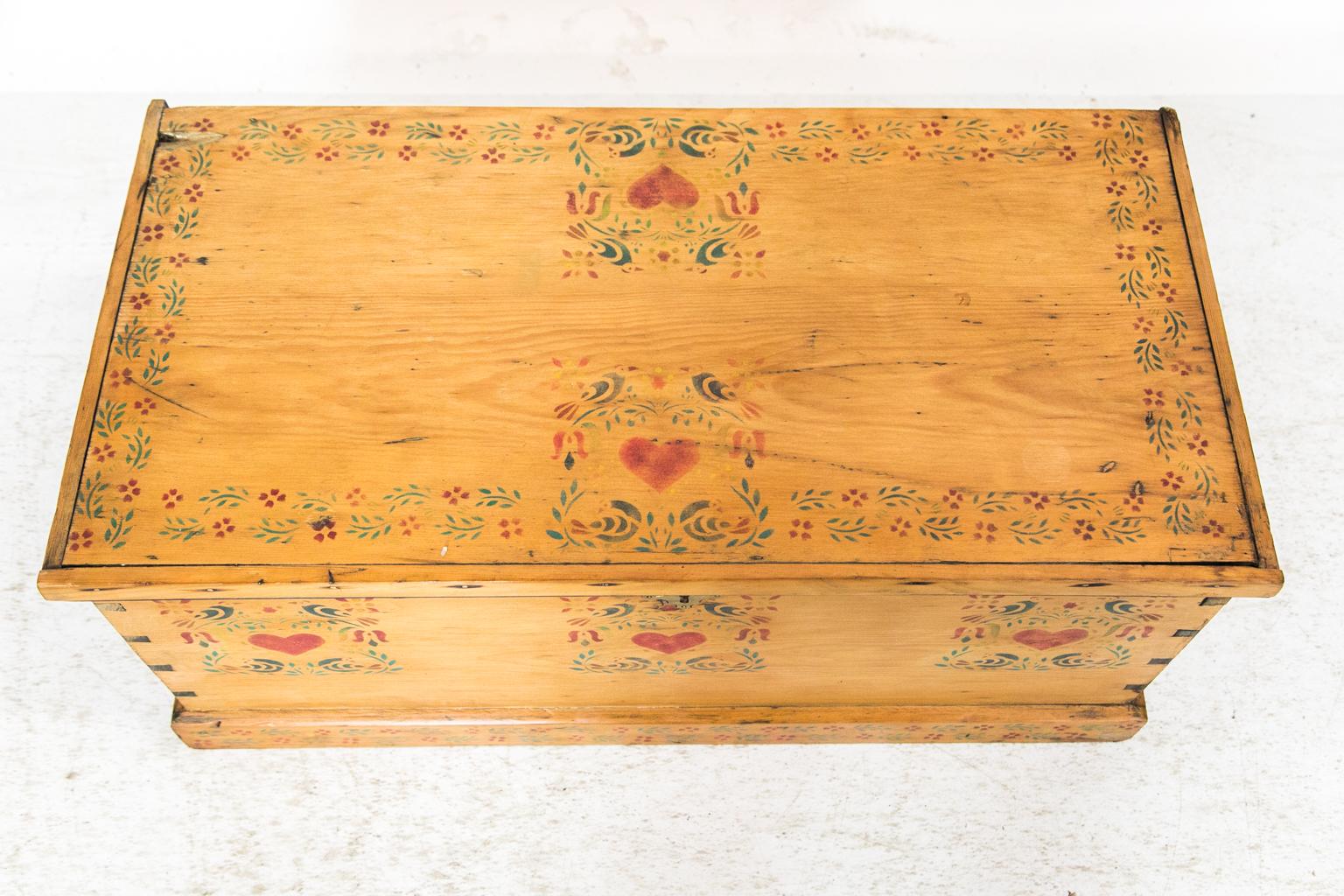 This blanket chest has exposed dovetail construction and is painted on the front and top with hearts and interlaced flowers and vines.