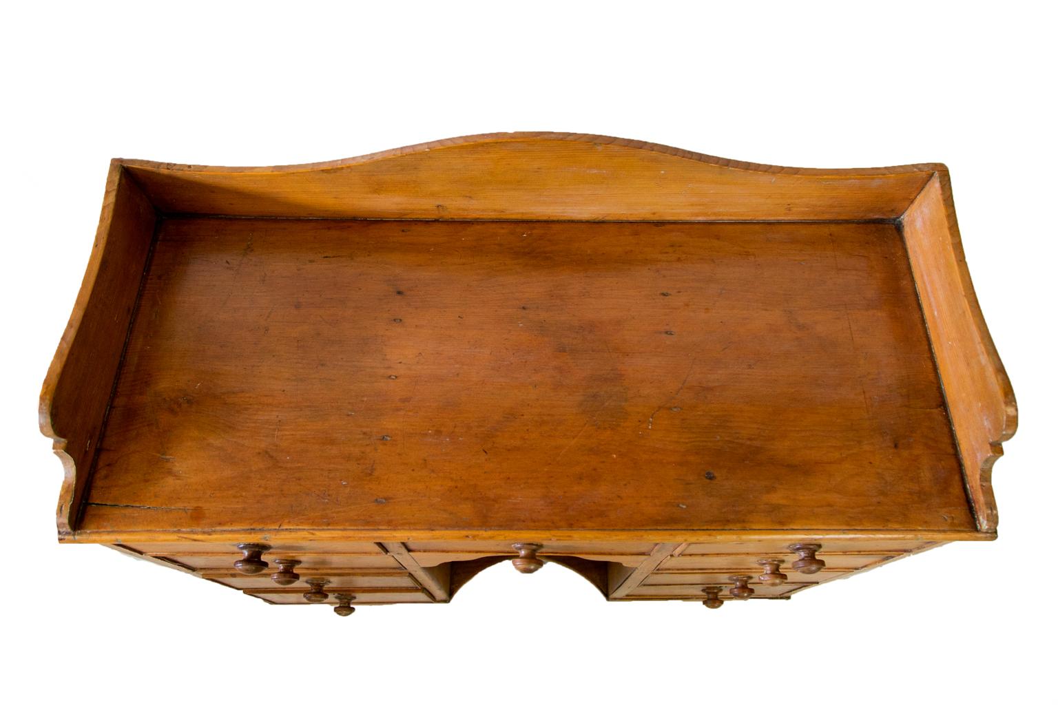 Server inglese in pino, ha nove cassetti con i pomelli originali in noce torniti a mano. La parte superiore presenta una galleria sagomata. Lo scomparto centrale ha una staffa ad arco sagomata e un ripiano inferiore concavo. I grembiuli laterali