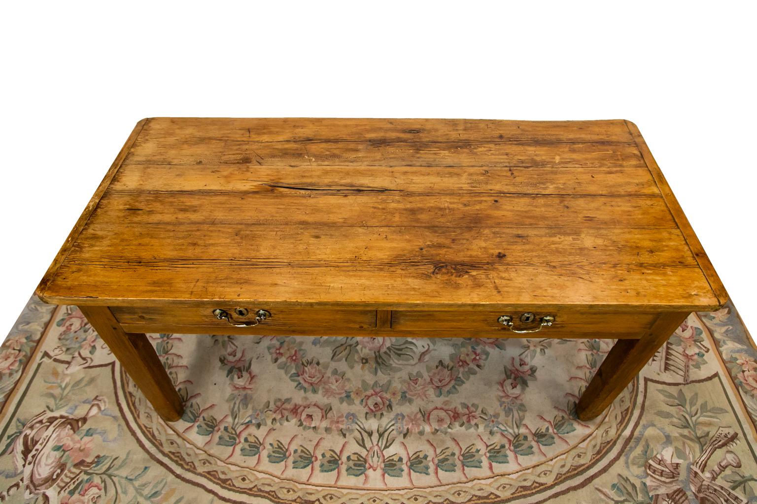The top of this table has weathered patina with shrinkage cracks in the cavities. There is exposed peg construction throughout. The top has 1 1/4 inch breadboard ends, each with three exposed mortise and tenon joints. The hardware is later.