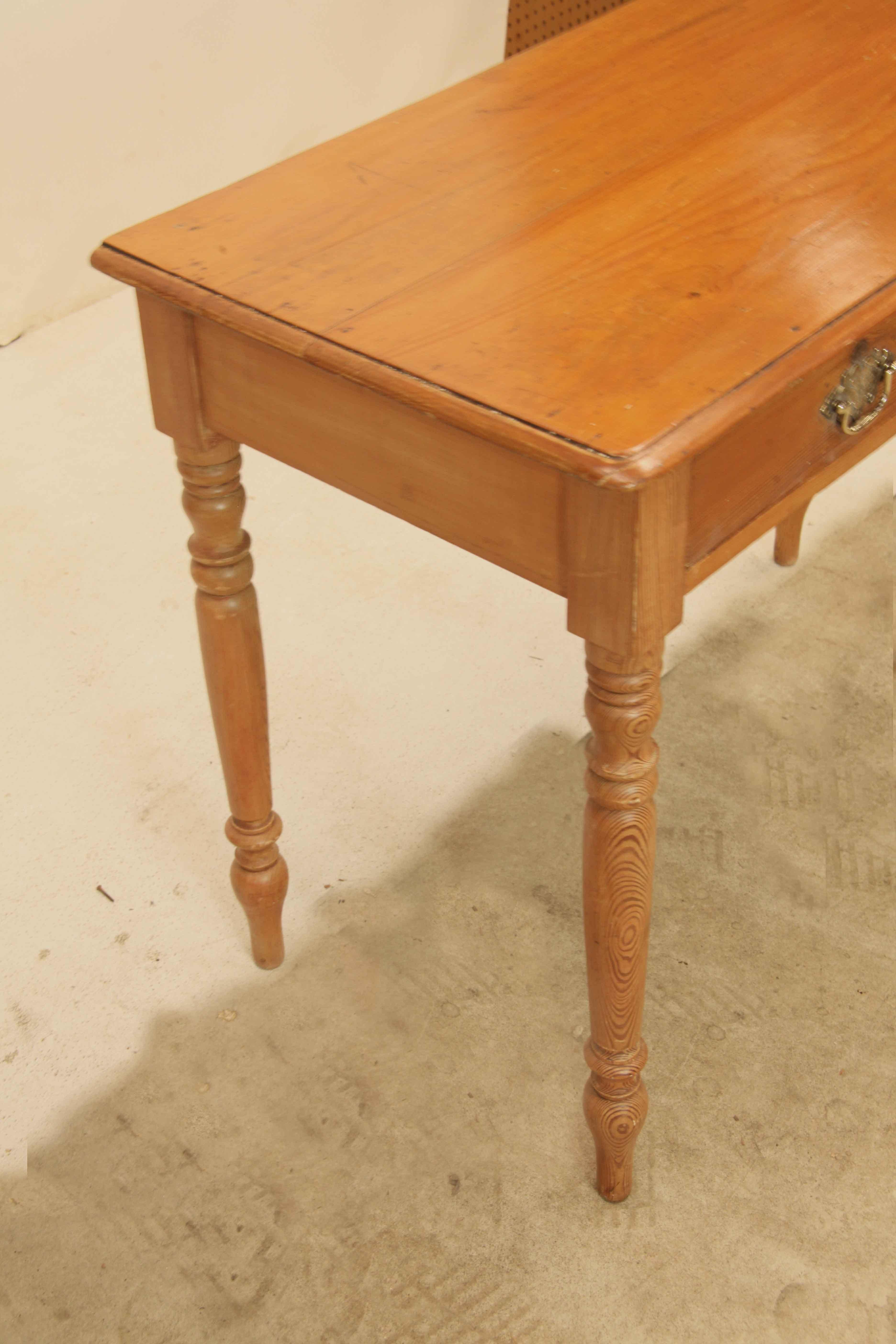 Mesa auxiliar de pino inglés con dos cajones,  esta mesa tiene un cálido color miel , los tiradores de los cajones con placas traseras grabadas.  Las patas tienen agradables torneados y están bien proporcionadas.  