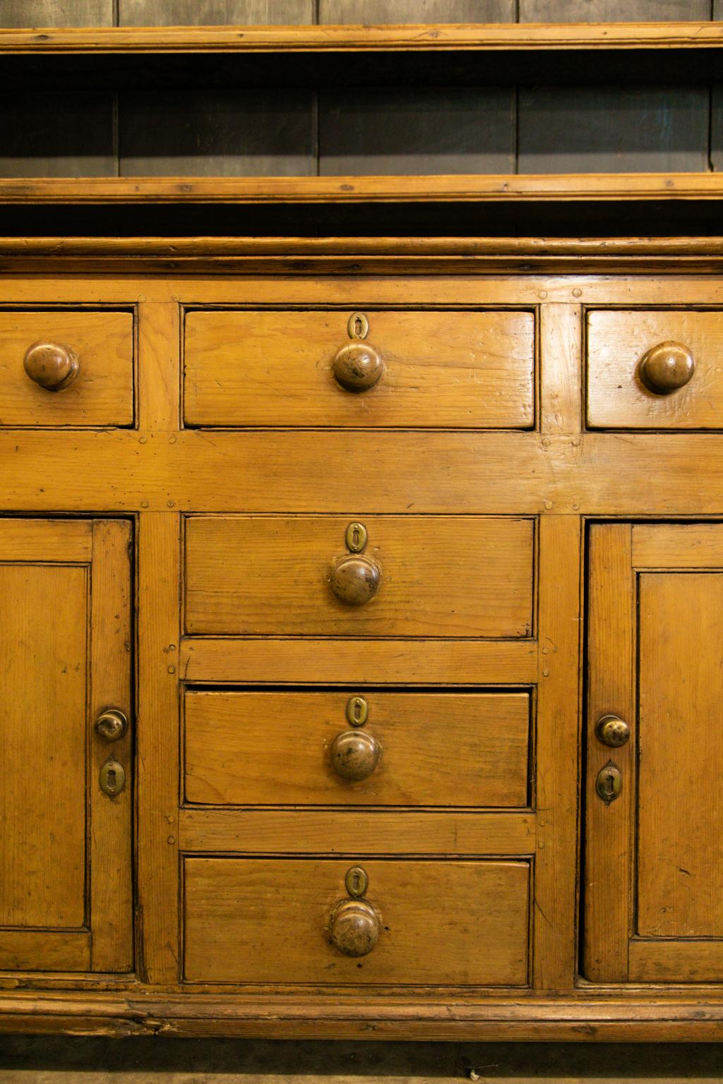 English pine welsh dresser has its original wooden knobs. The top has fixed plate rails, but these could be removed. There are six working drawers and two doors in the lower half.
   