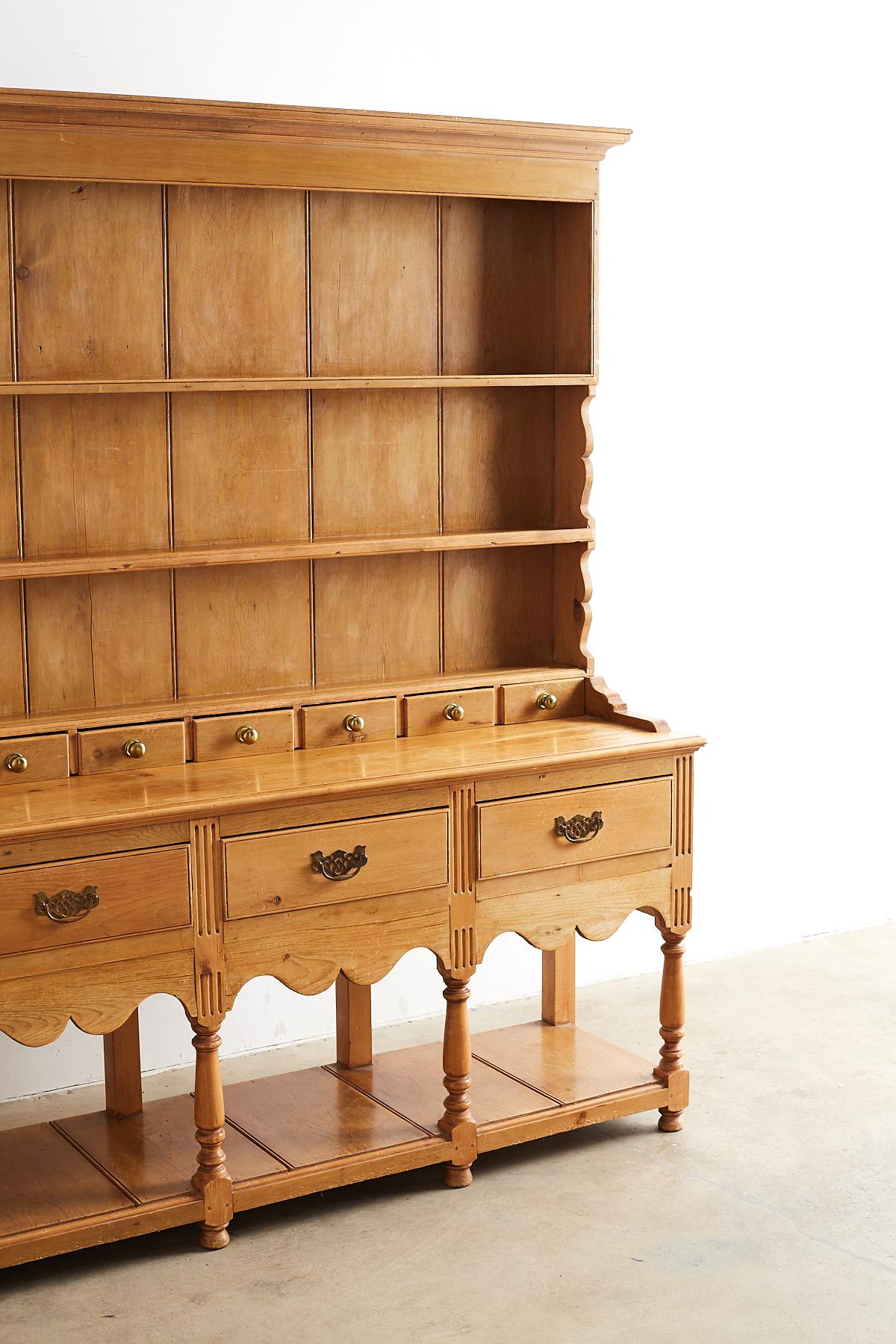 Grand English pine Welsh dresser or sideboard with a pot board and rack. Featuring a large rack with a row of nine small drawers in a row having large brass ball pulls. The generous dresser is fronted by four large drawers each with a brass handle