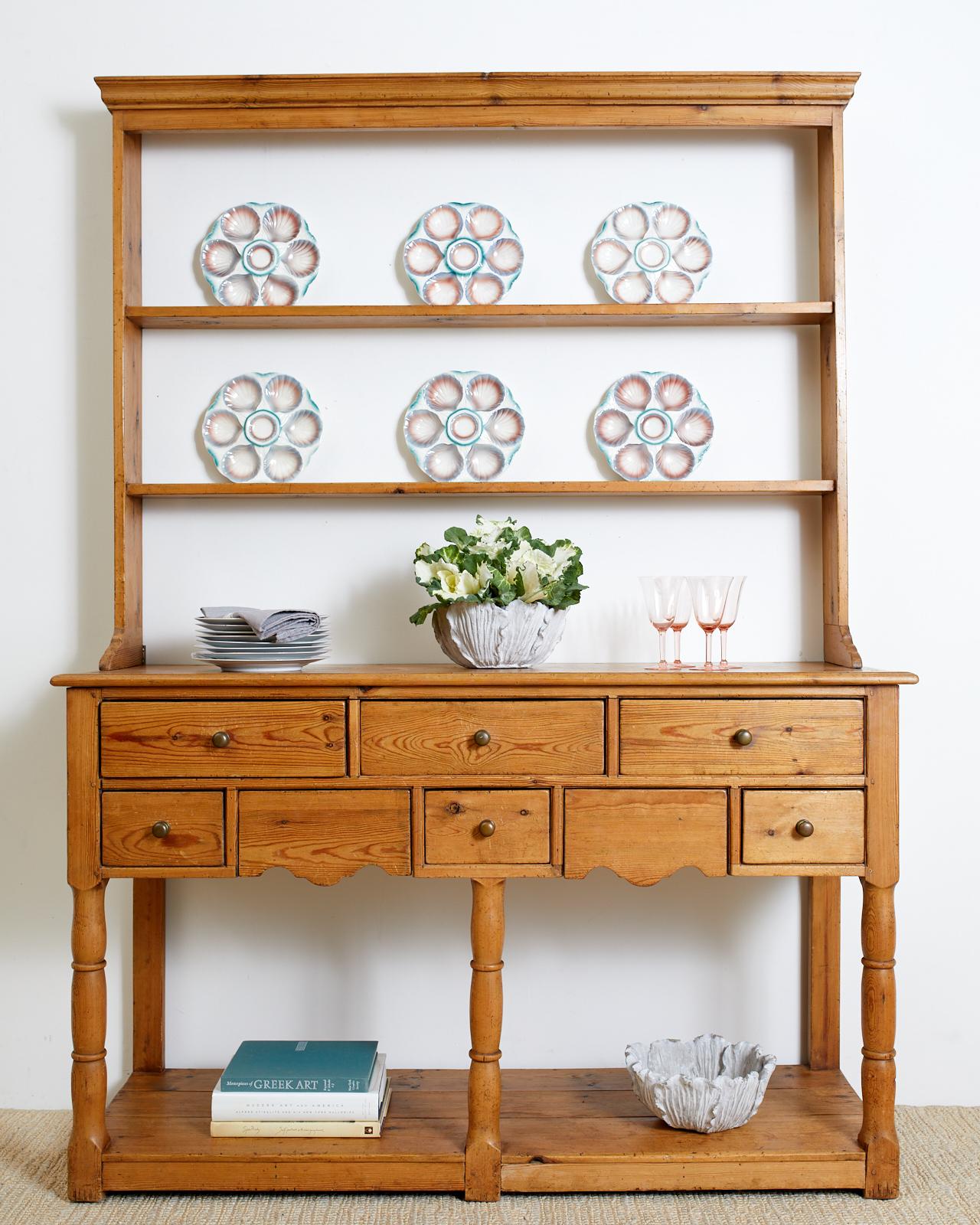 Rustic country English welsh dresser or cupboard with a pot board base and upper rack having a molded cornice above a two shelf dish rack. The sideboard is fronted by eight drawers, six with brass pulls and two hidden with serpentine shaped bottoms.