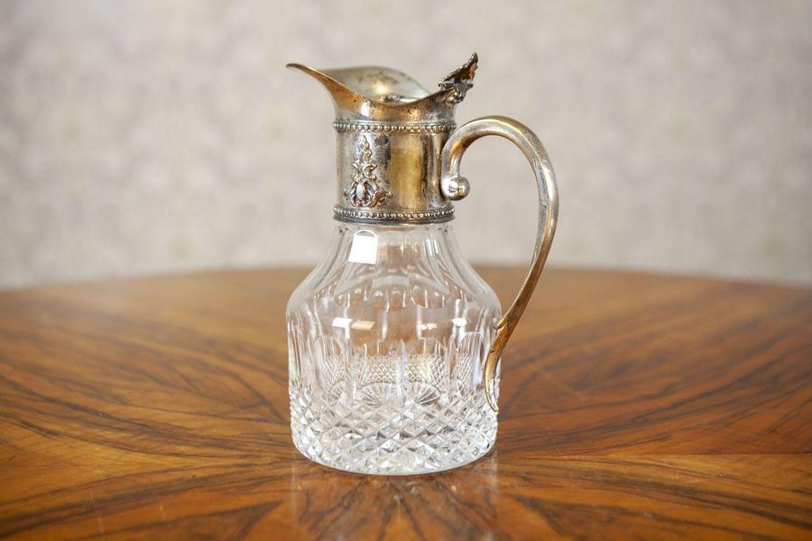 English Pitcher With Silver-Plated Handle From the Turn of the 19th and 20th Centuries

A lidded English pitcher made of crystal glass, featuring a silver-plated handle and fittings adorned with a floral motif, dated to the turn of the 19th and 20th