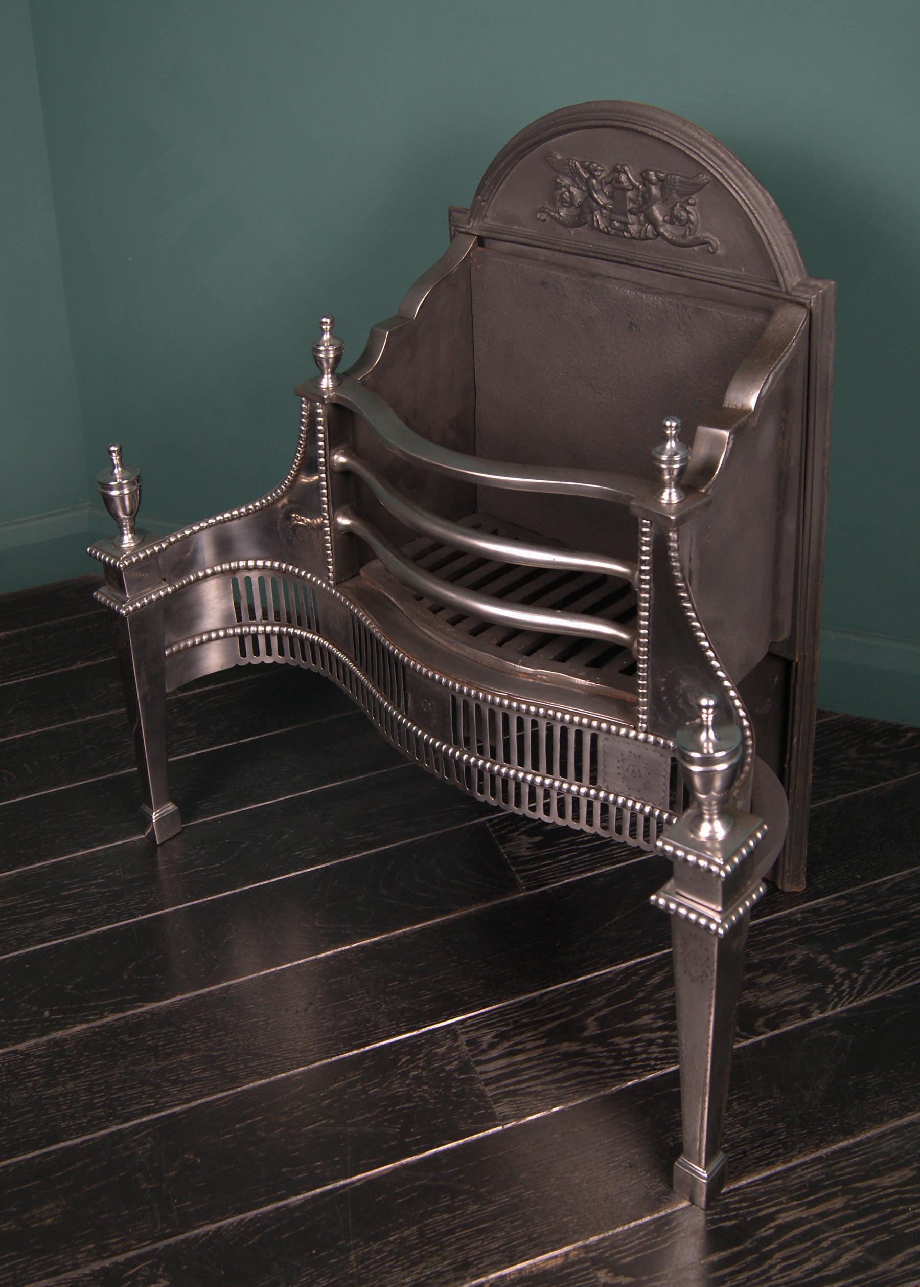 An English polished steel Adam-Style dog grate by Thomas Elsley with railed serpentine basket set above a fluted fret frieze interrupted with square plaques with engraved oval and flower.  This is flanked by square tapering legs with urn finials