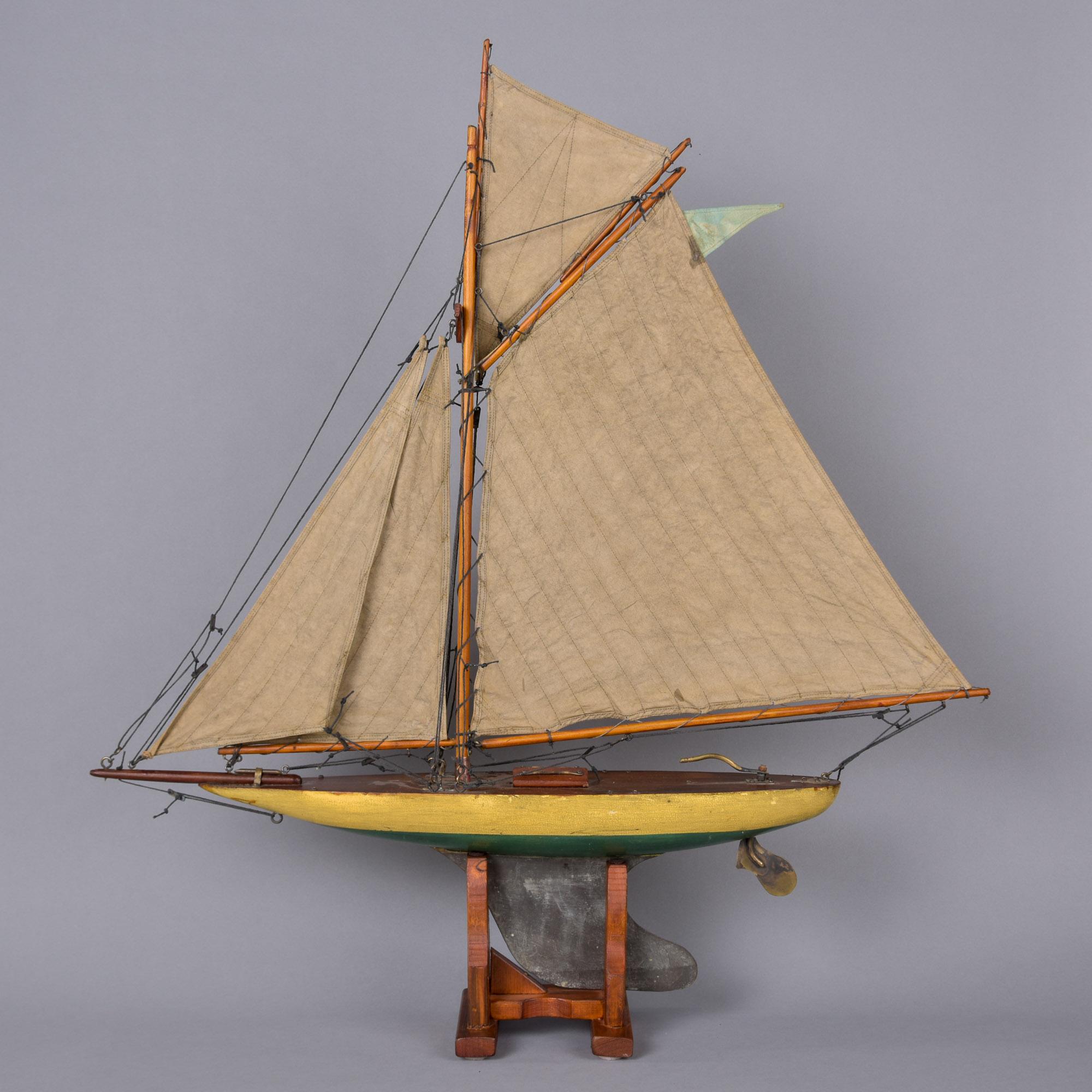 Trovata in Inghilterra, questa barca da laghetto in legno fatta a mano con vele originali in stoffa risale agli anni '40. Si tratta di una barca a vela con un solo albero - crediamo sia uno sloop - e presenta uno sprito di prua, dettagli in ottone e