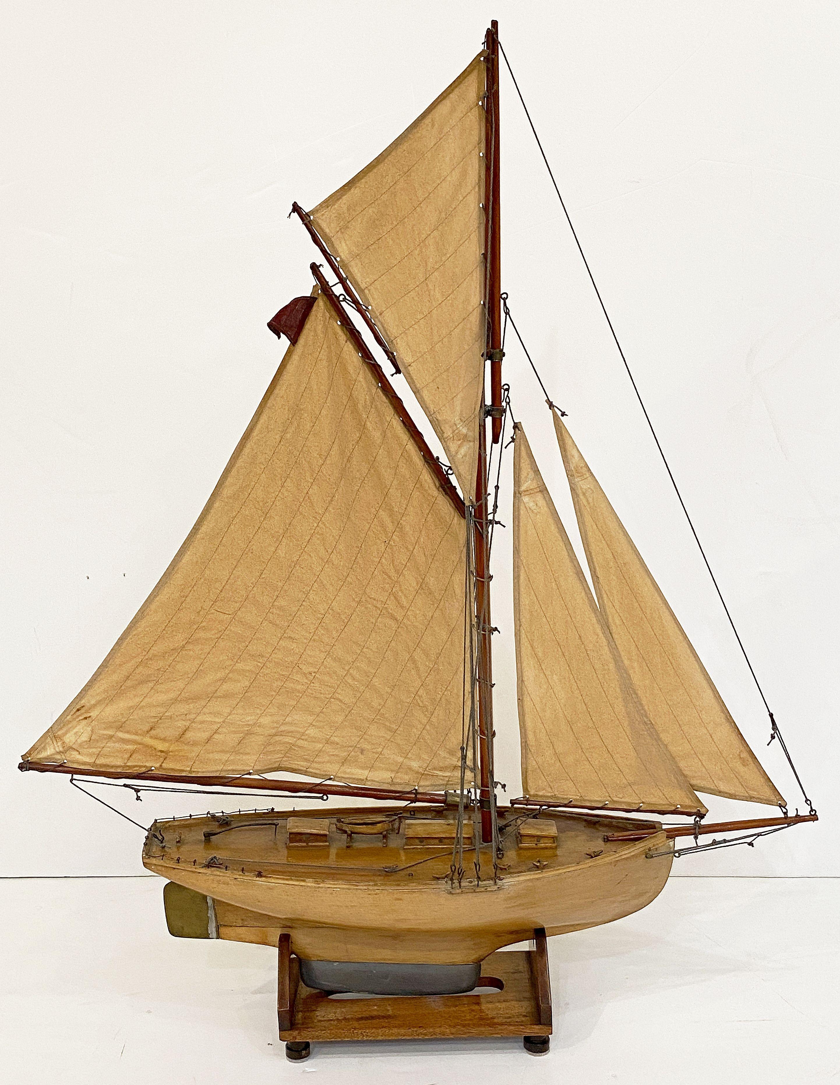 A handsome English pond yacht from the Edwardian era, handcrafted from wood and brass and featuring vintage cloth sails and fittings.

Displayed on a separate, custom-fitted stand.

Height and depth includes the stand.

Dimensions: H 41 1/2