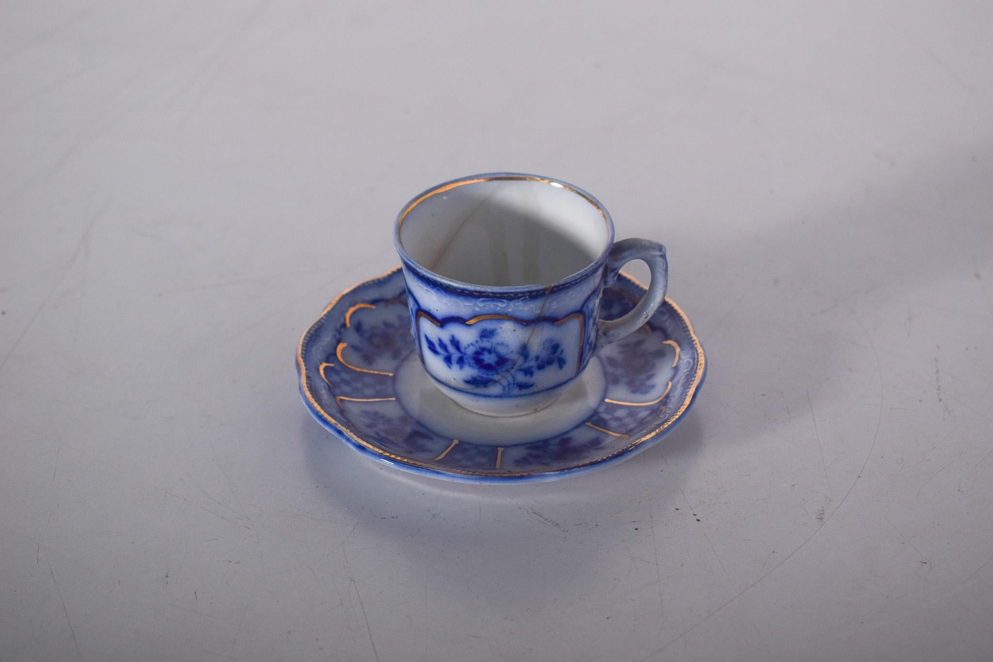 Tasse et soucoupe en porcelaine anglaise. Charmante décoration dans les tons de bleu et détails dorés. La tasse présente un élégant motif floral peint à la main, avec des fleurs bleu cobalt soulignées par des contours dorés qui ajoutent une touche