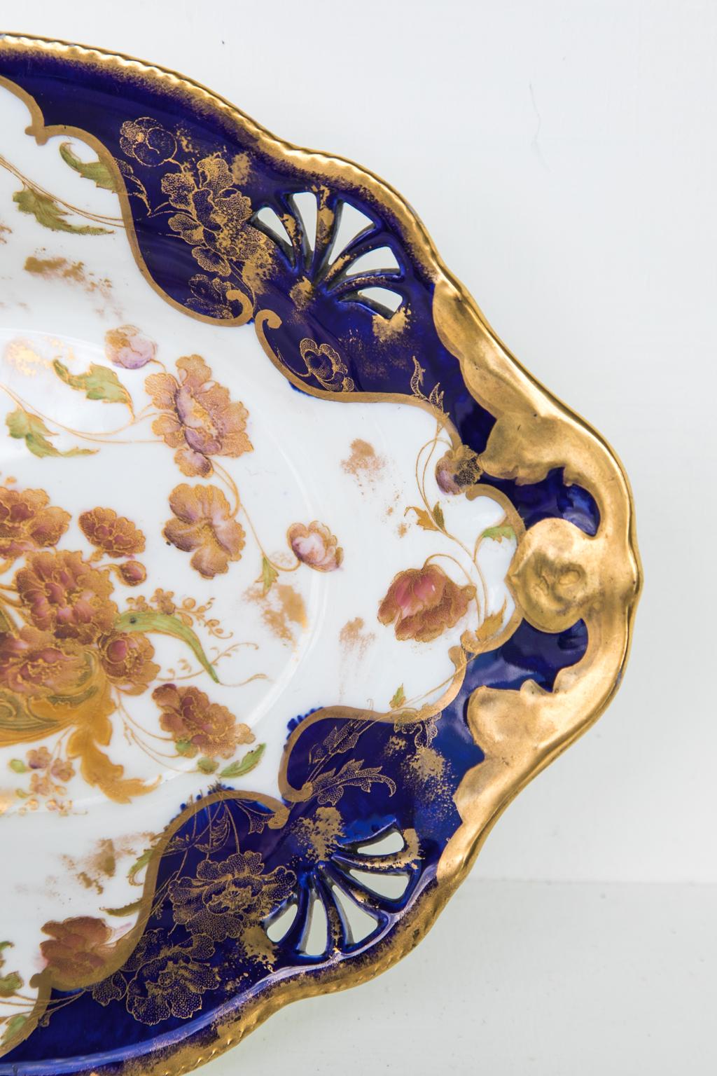 English porcelain dish, with reticulated bands and gilt floral work in the cobalt rim. The center is decorated with floral and arabesque motifs.
        
