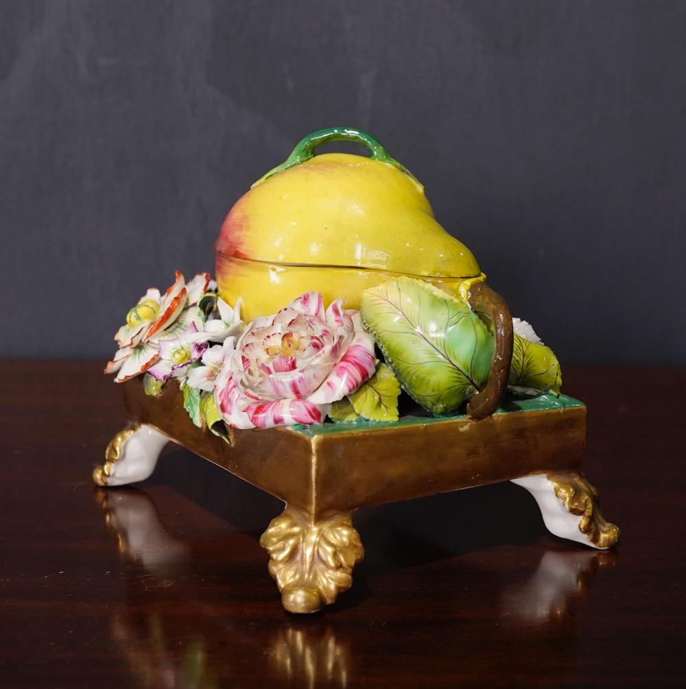 Unusual English porcelain inkwell, modelled as a ripe pear opening to reveal a separate inkpot and small lid with flower knop, the rectangular gilt plinth encrusted with life-size, lifelike flowers, standing on four tall acanthus leaf feet to the