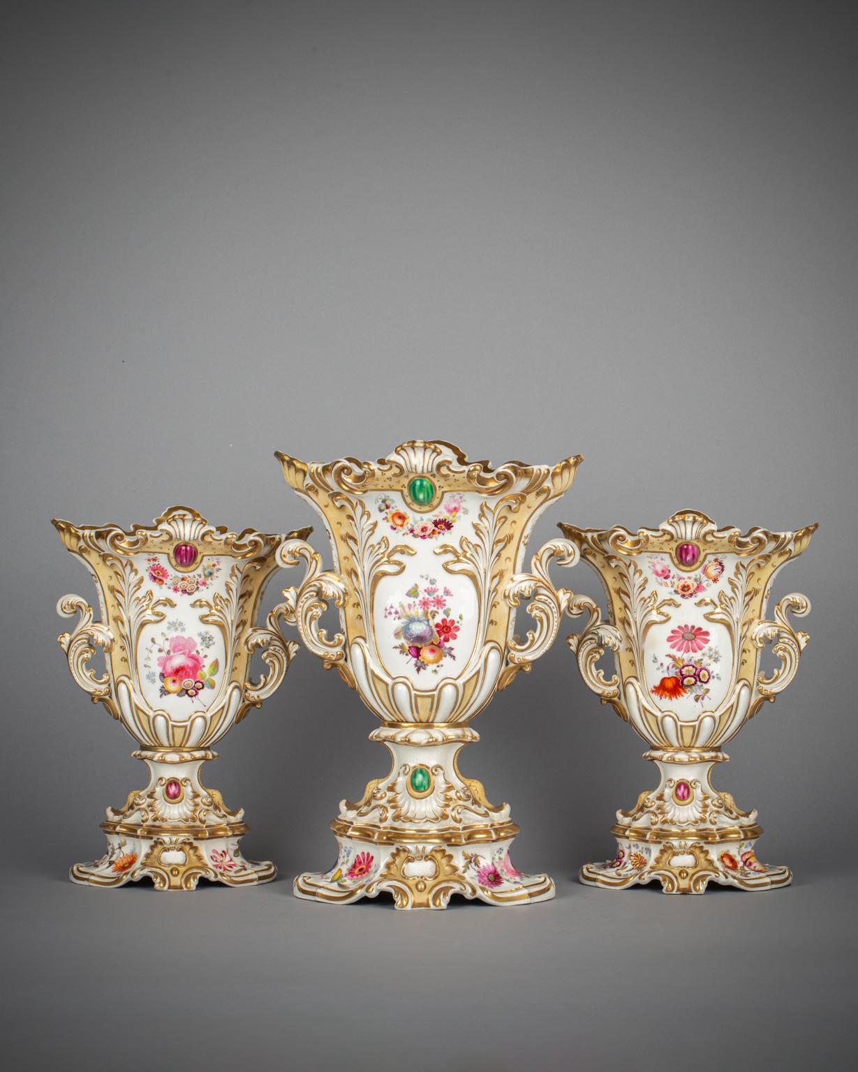 The colored reserves painted with a floral still life, the reverse with sprays of flowers. The bases similarly painted. With molded, gilded scrollwork and 