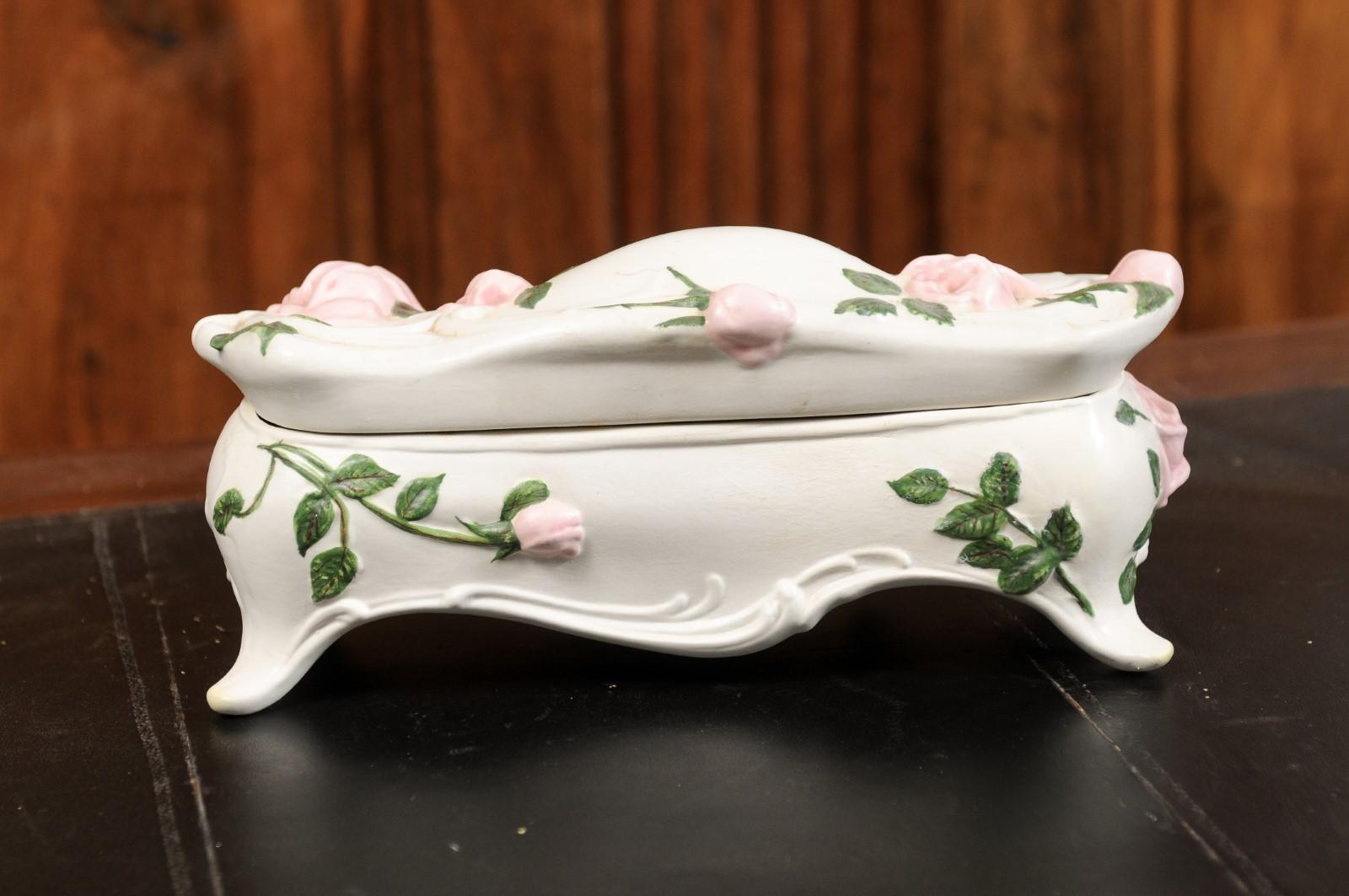 An English porcelain vanity box from the 20th century, with painted roses and lid. Created in England, this porcelain vanity box features sinuous Rococo style lines perfectly accented with pink roses and green foliage, standing out beautifully on a